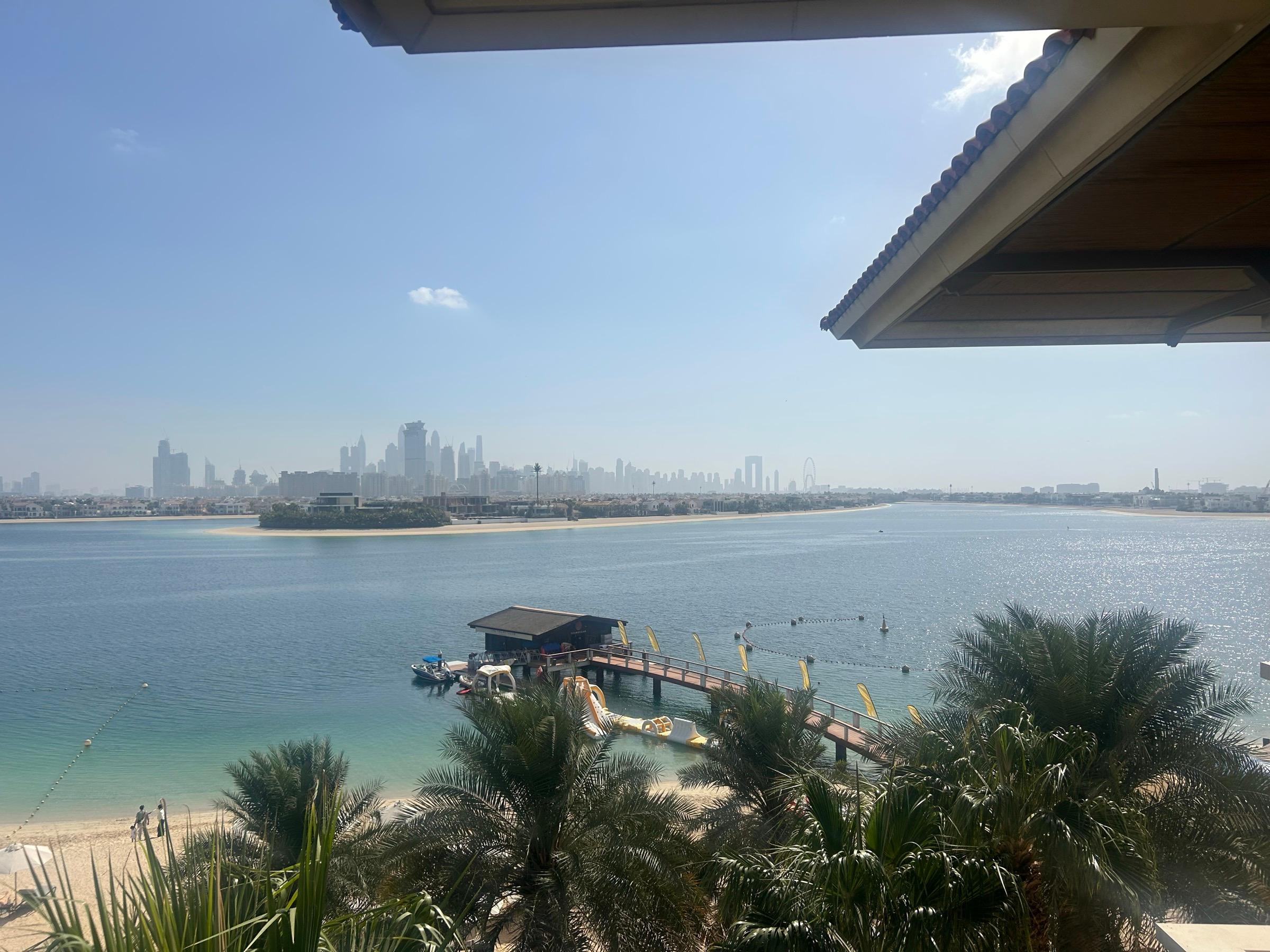 The Dubai skyline across the water from the Palm Jumeirah, with palms and a jetty in the foreground