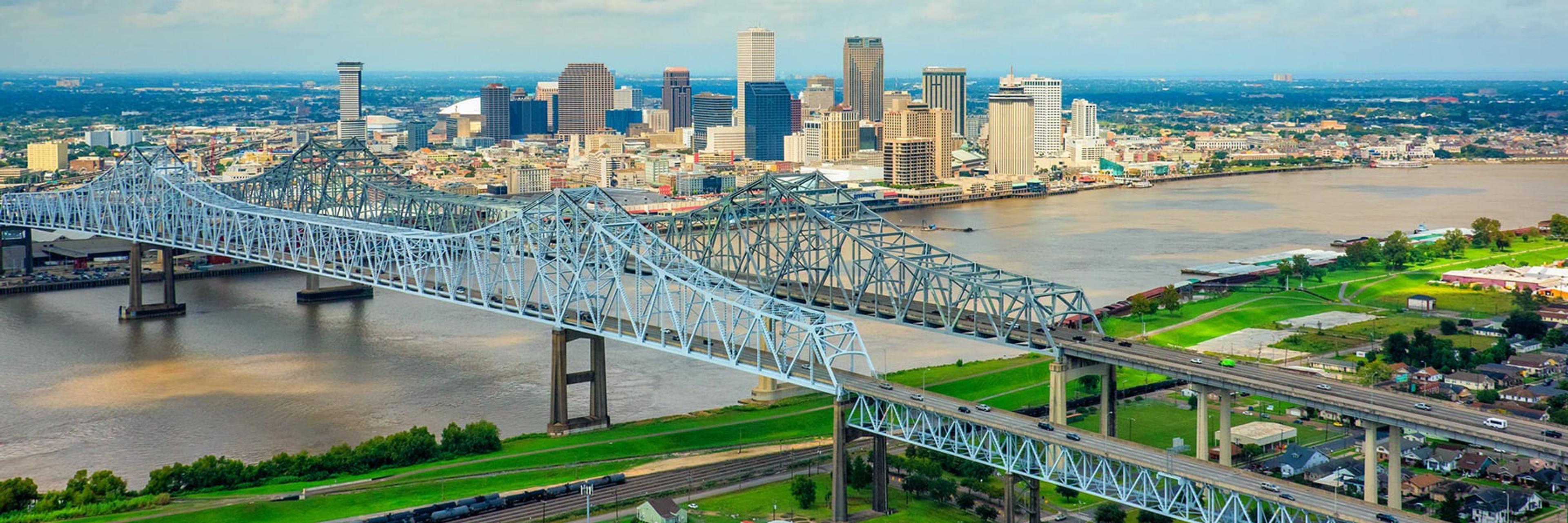 An aerial view of New Orleans showing a bridge crossing the Mississippi River with the downtown skyline beyond.