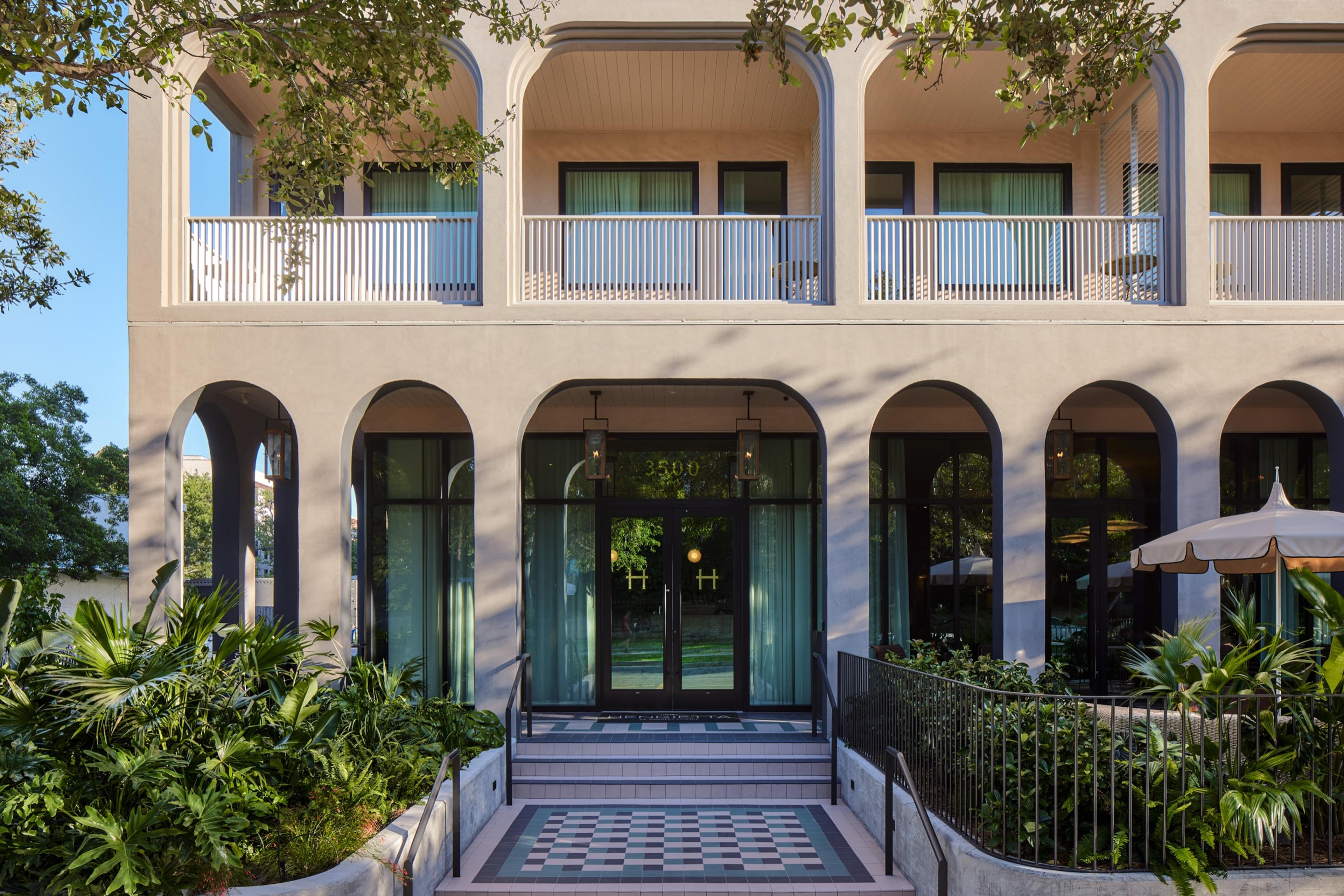 The entrance of a pale stucco building: glass doors under an arch with two lanterns hanging above, a checked tiled step, and balconies above.