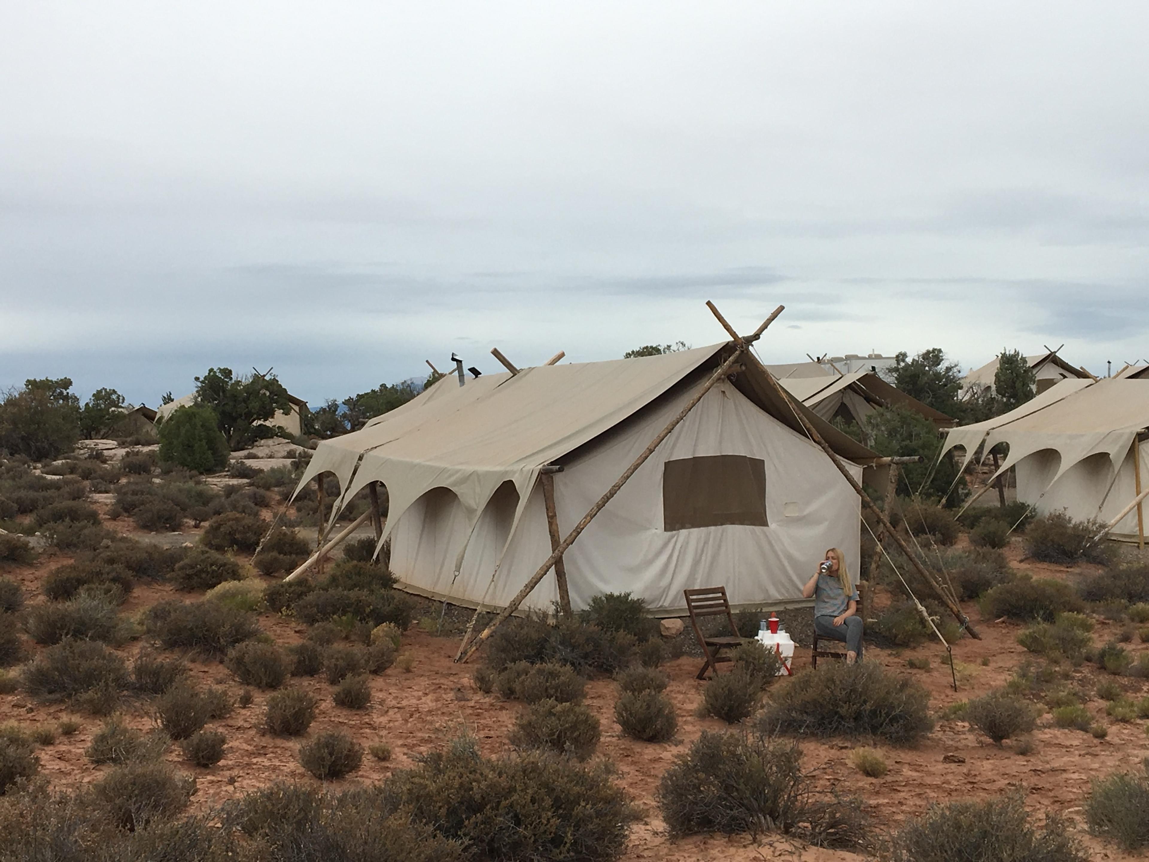 A canvas safari tent on a timber frame among desert scrub, under a pale sky