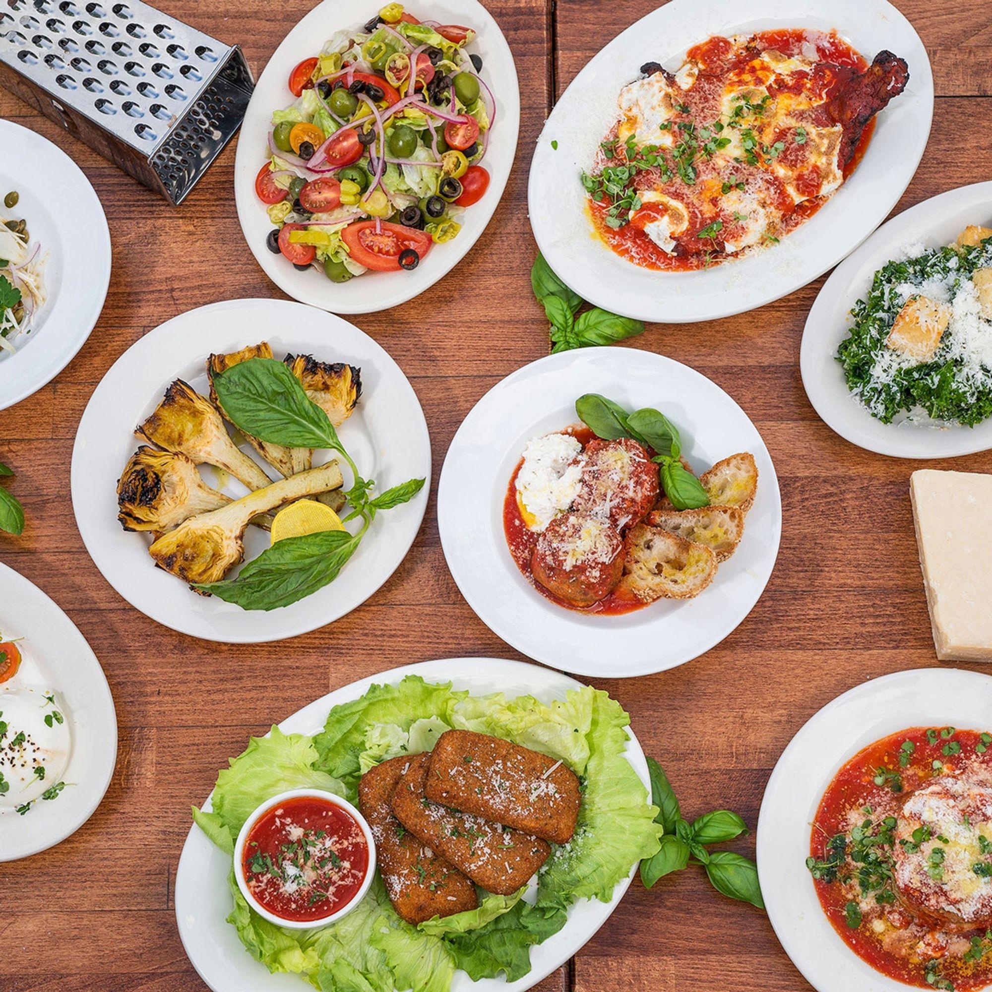 Plates of grilled artichoke and other dishes on a wooden table, seen from above