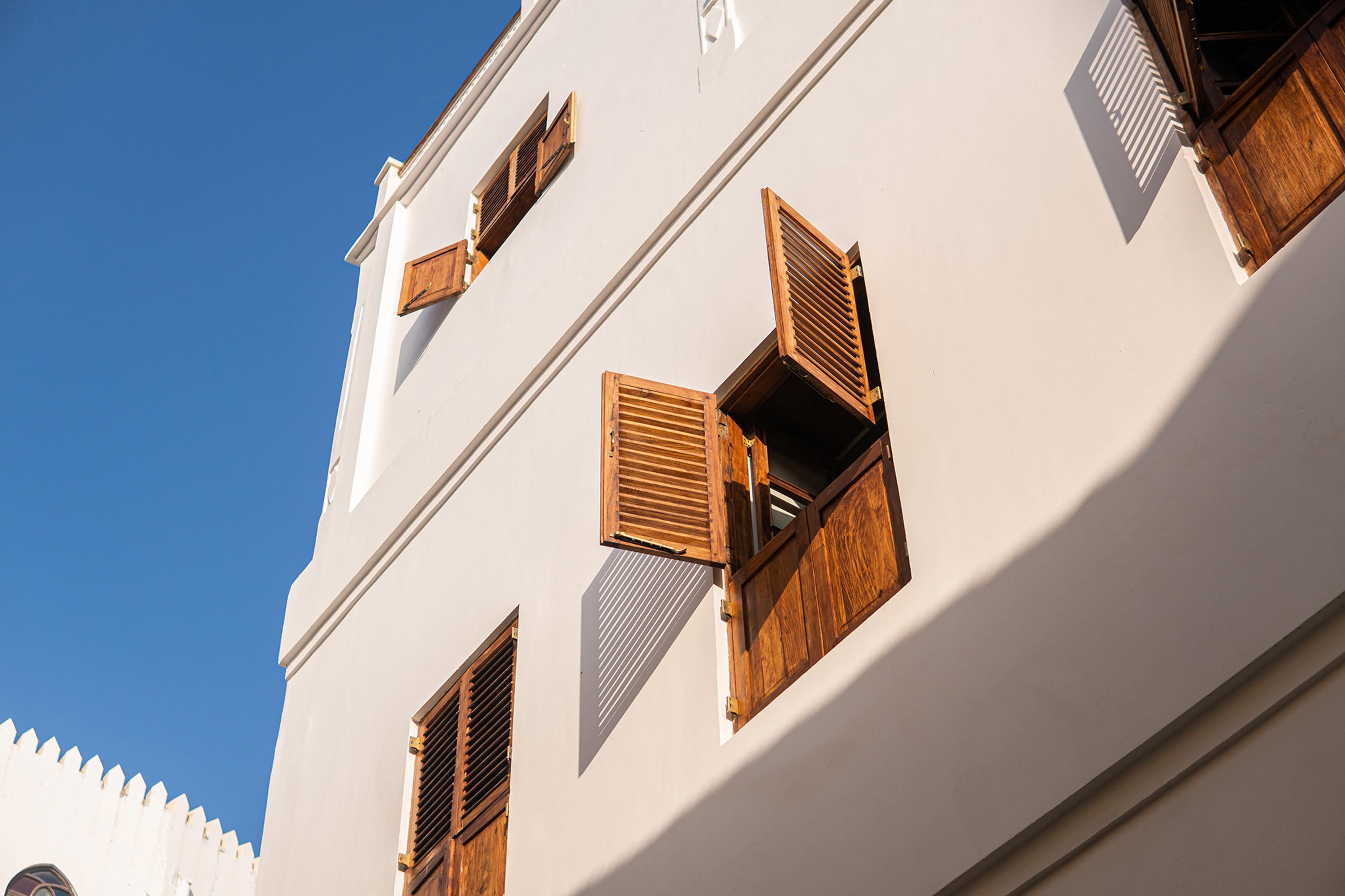 A white building facade with open wooden shutters, photographed from below against a blue sky.