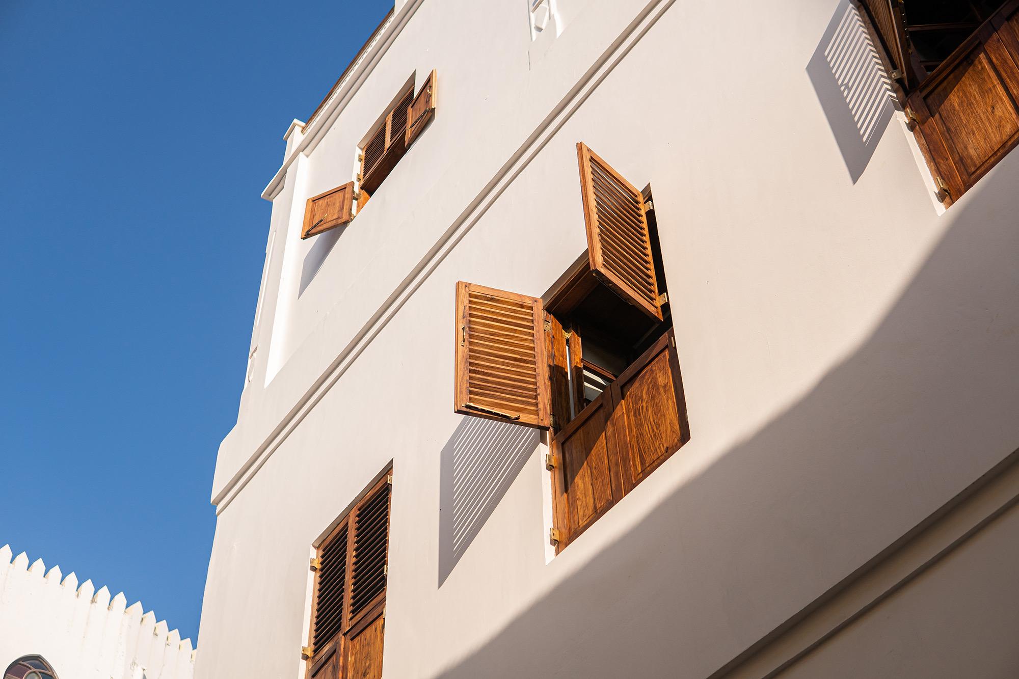 A white building facade with open wooden shutters, photographed from below against a blue sky.