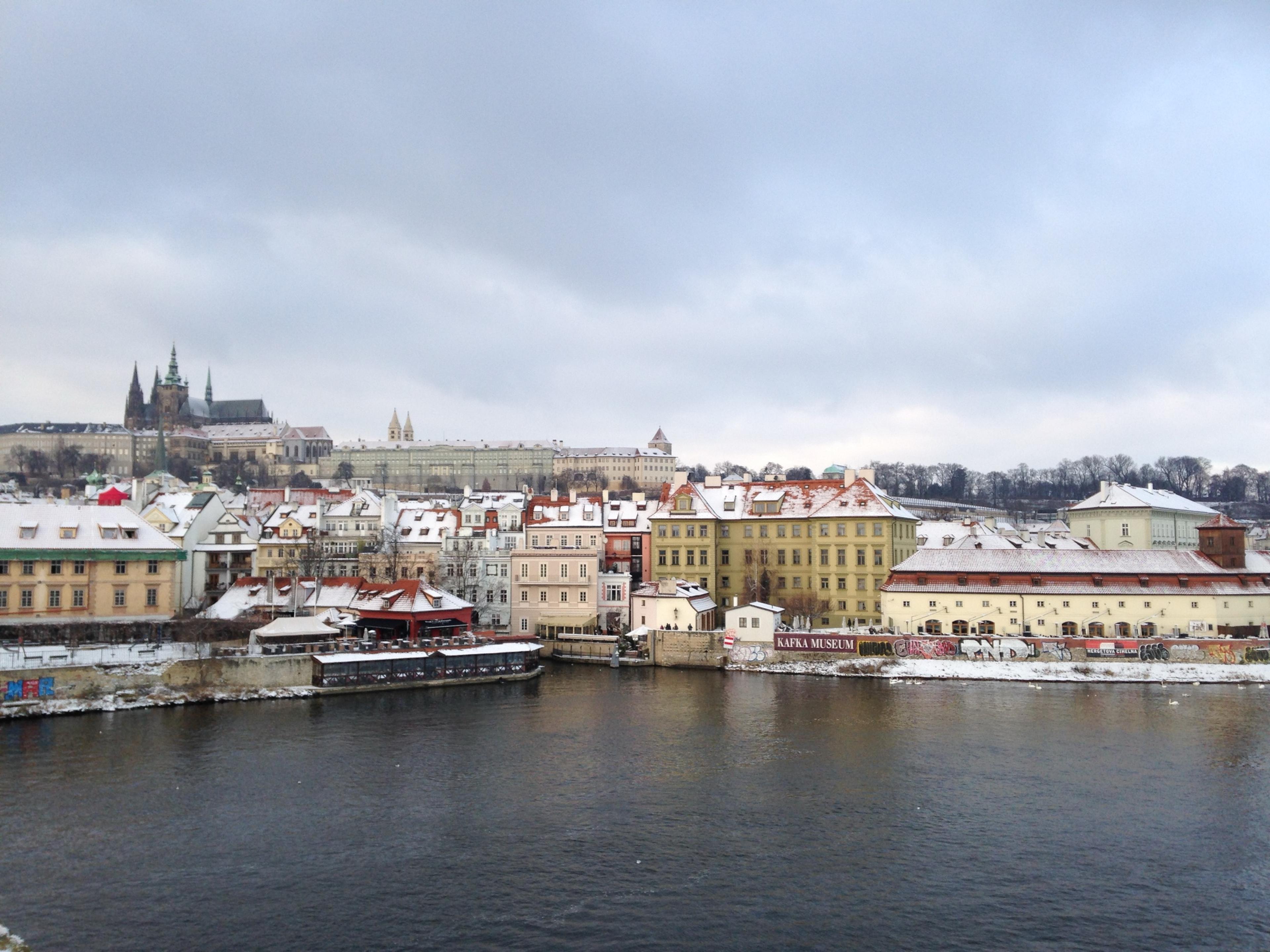 Prague Castle and St Vitus Cathedral above snow-covered roofs, across the Vltava in winter