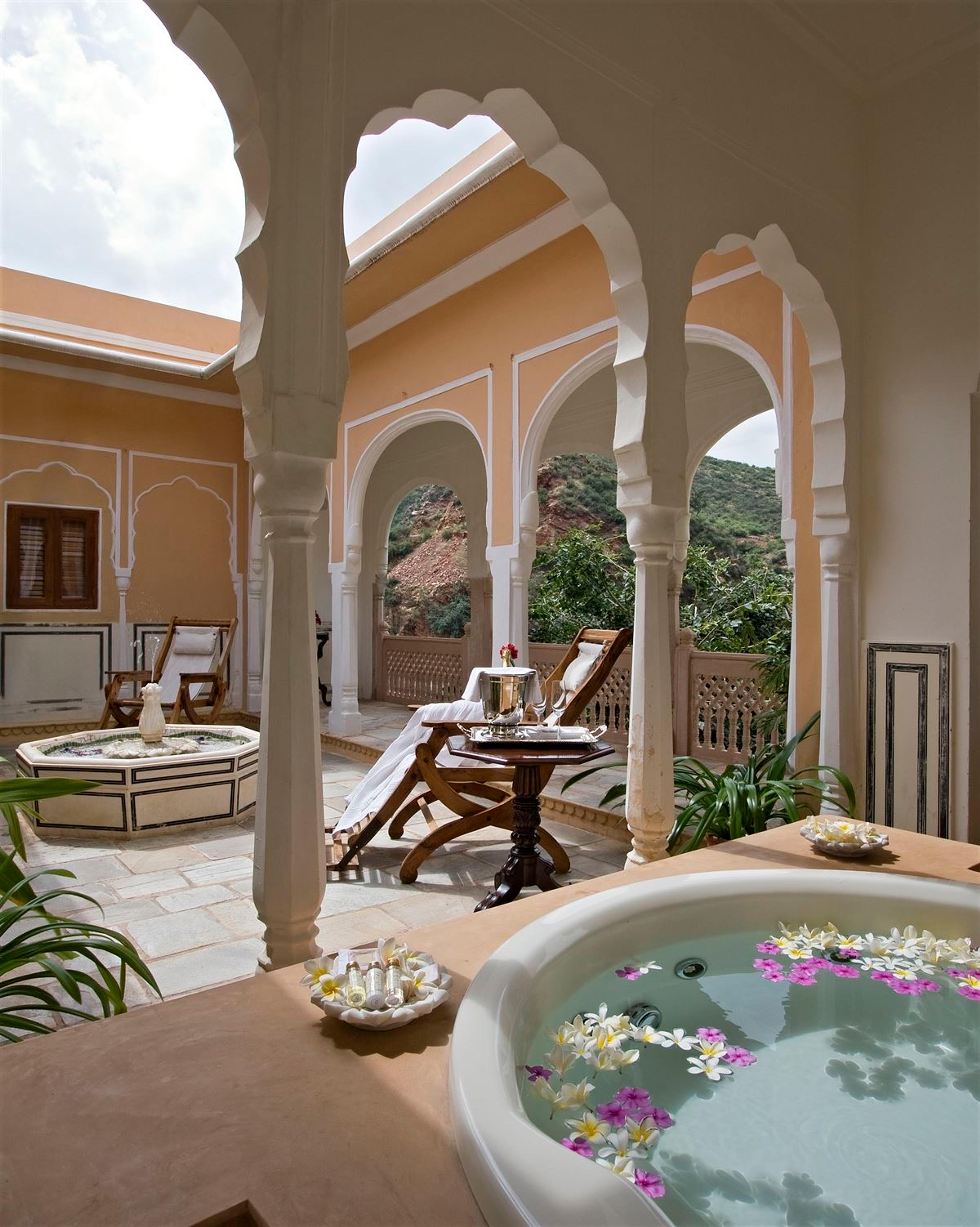 A small round plunge pool on a covered terrace with sun loungers and hills visible beyond the arches.