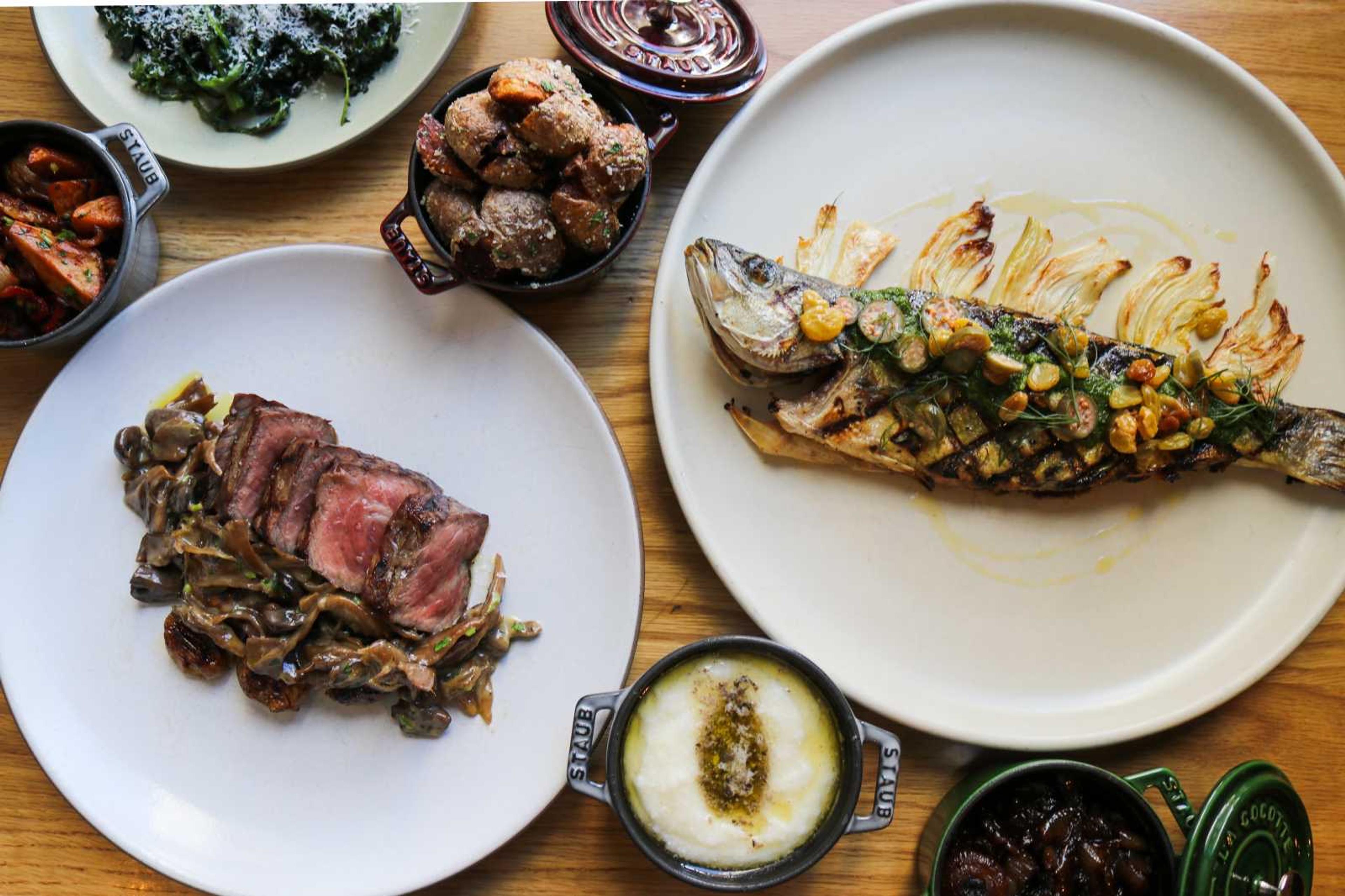 Steak, a whole grilled fish and sides on the table at Tavernetta