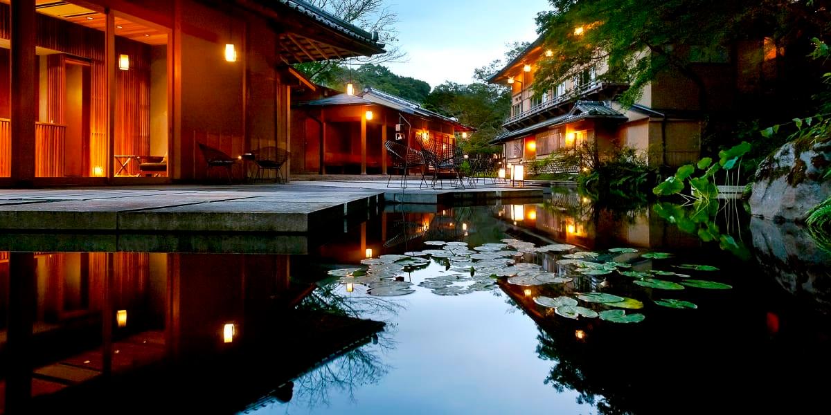 Hoshinoya Kyoto's wooden buildings lit at dusk and reflected in a lily pond