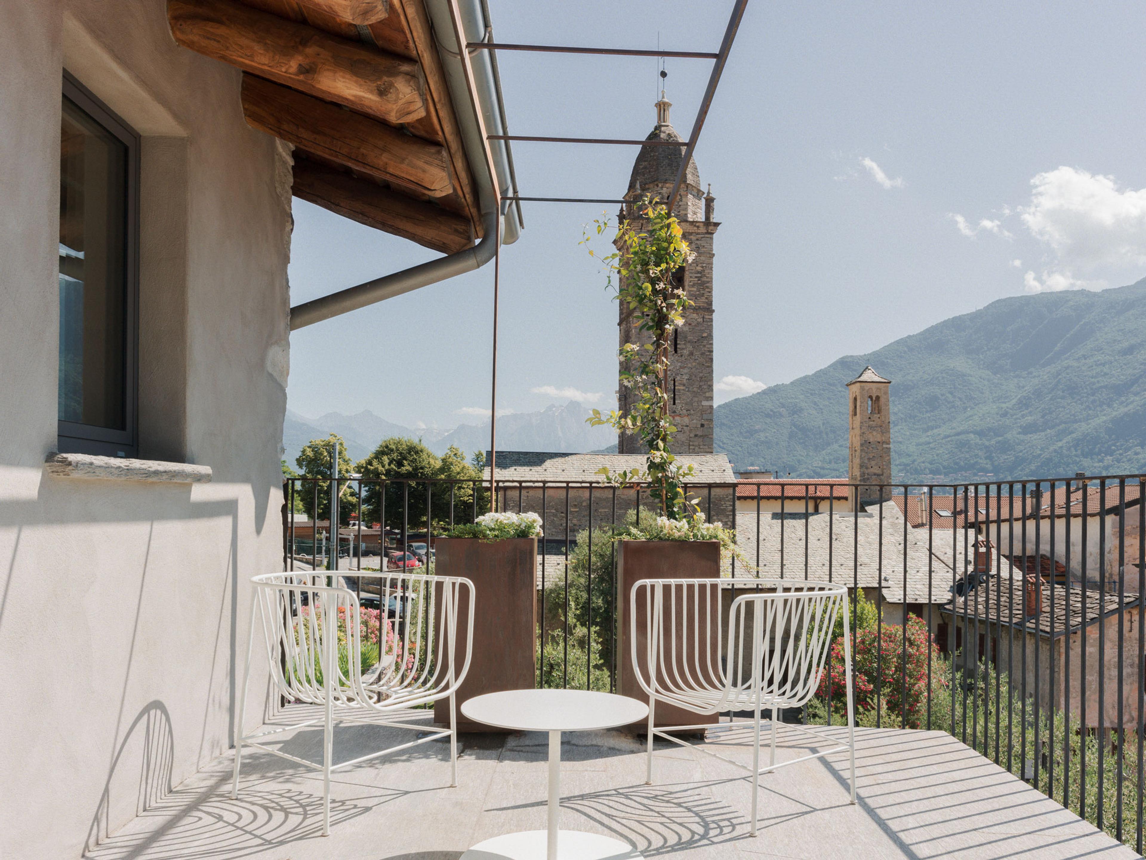 white wire chairs around a side table on a rooftop terrace, looking out at a bell tower and the mountains beyond