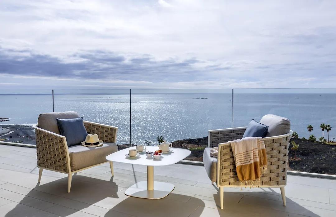 Two woven armchairs and a low table with coffee cups on a terrace above the sea