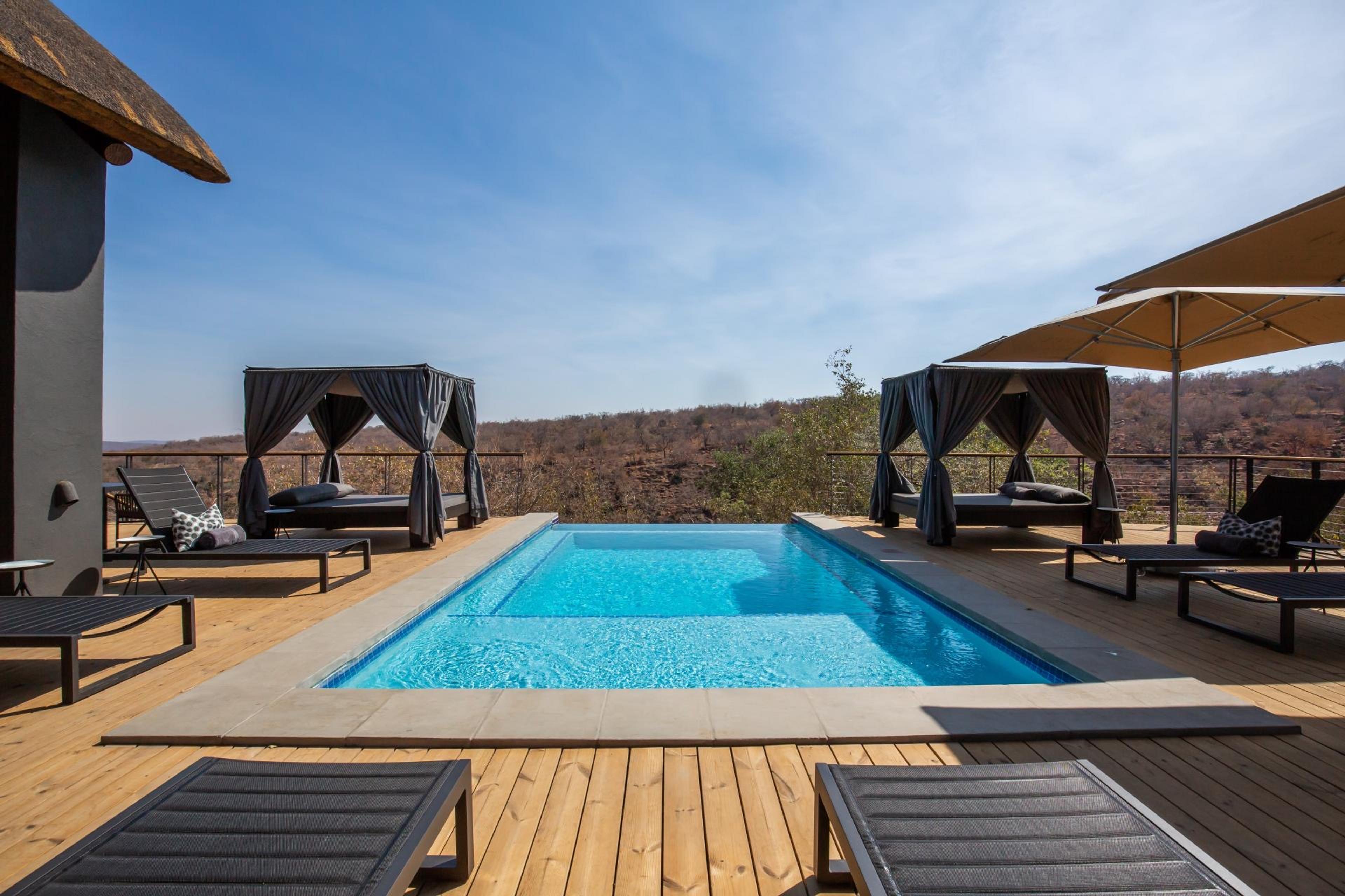The pool deck at 57 Waterberg in full sun, curtained daybeds either side of the pool and the bush running away to the hills
