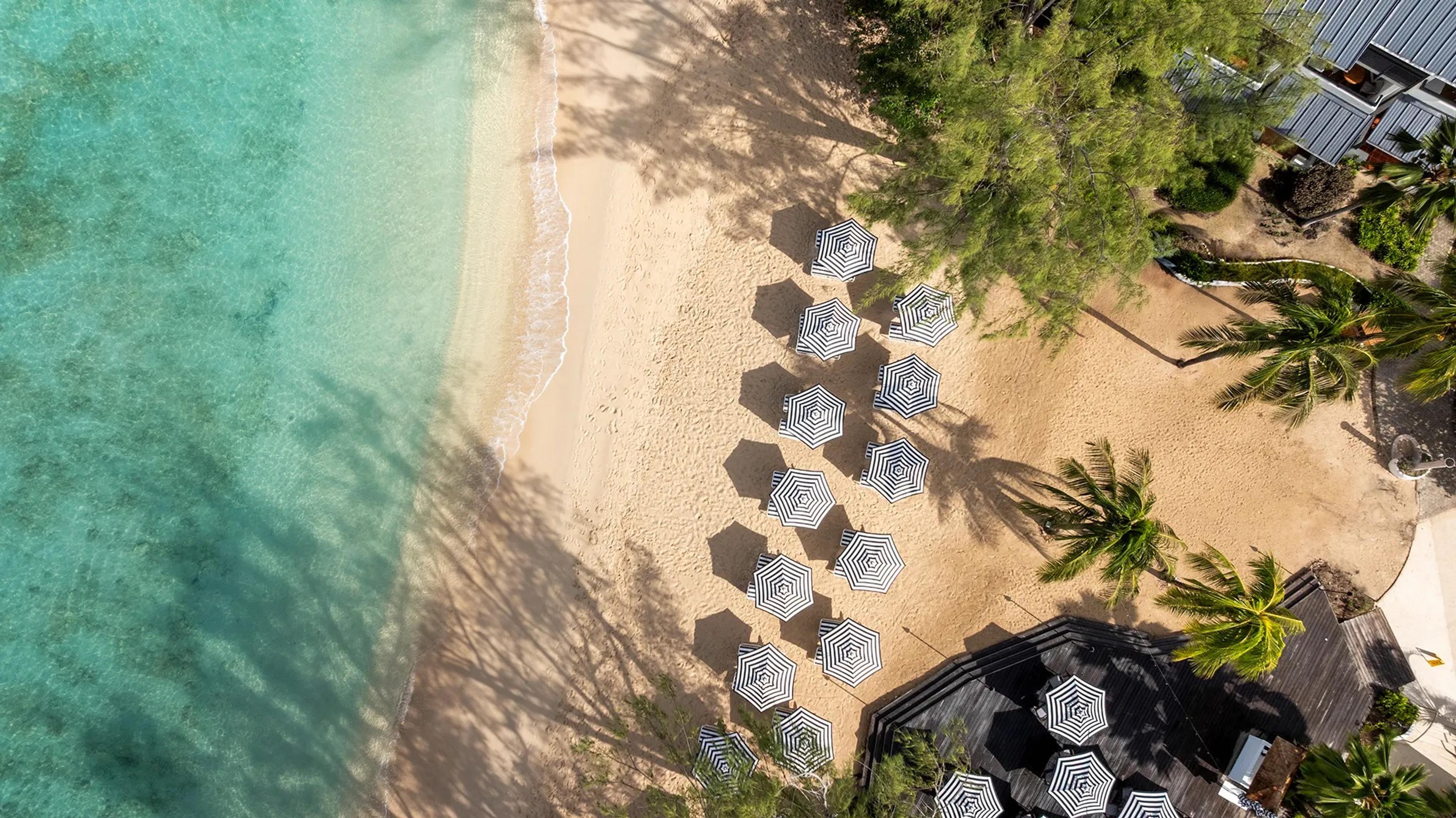 Striped parasols on the sand beside clear turquoise water, seen from above