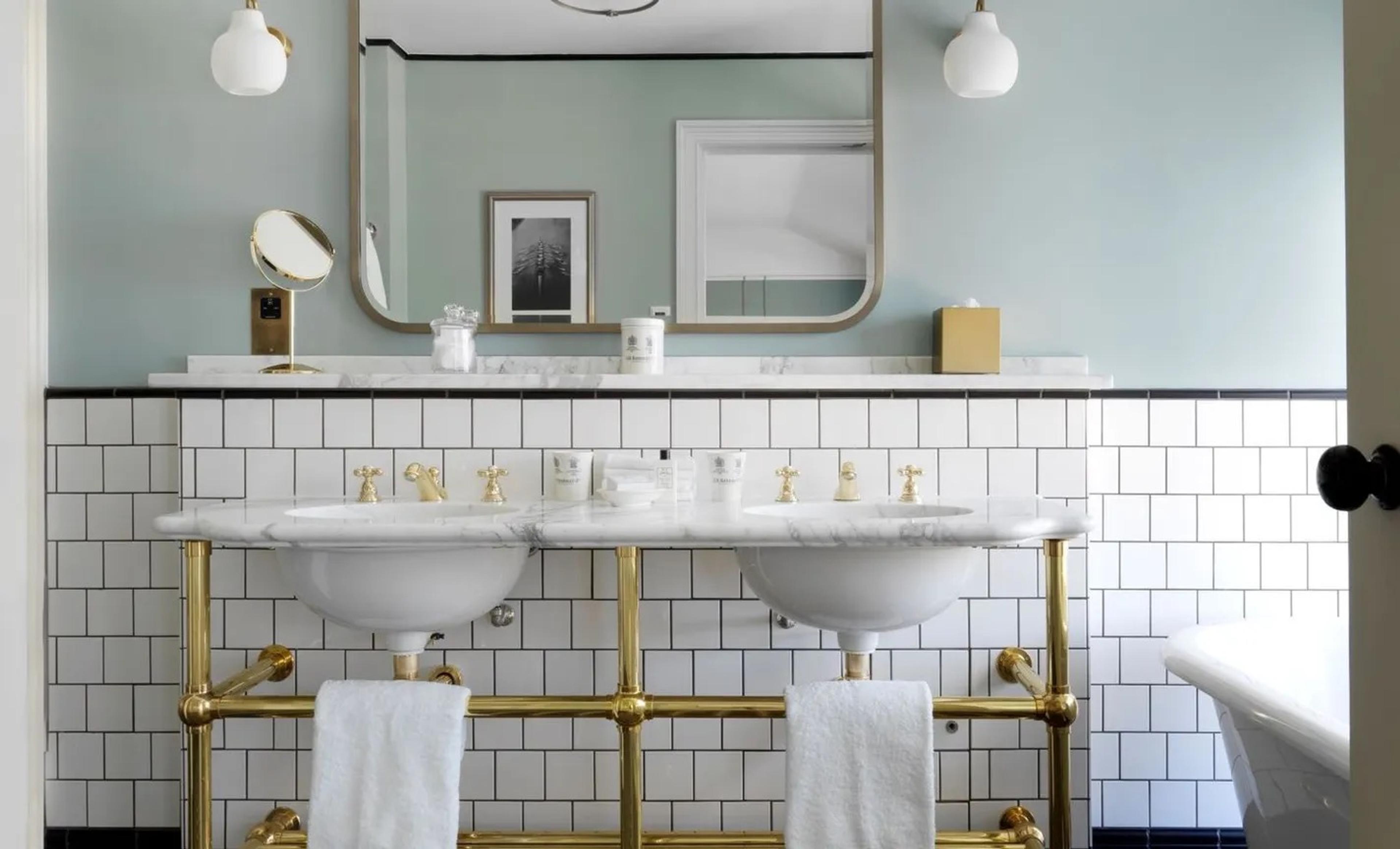 a bathroom with a white marble double vanity on brass legs, two round basins, a large arched mirror, and white hand towels hanging below