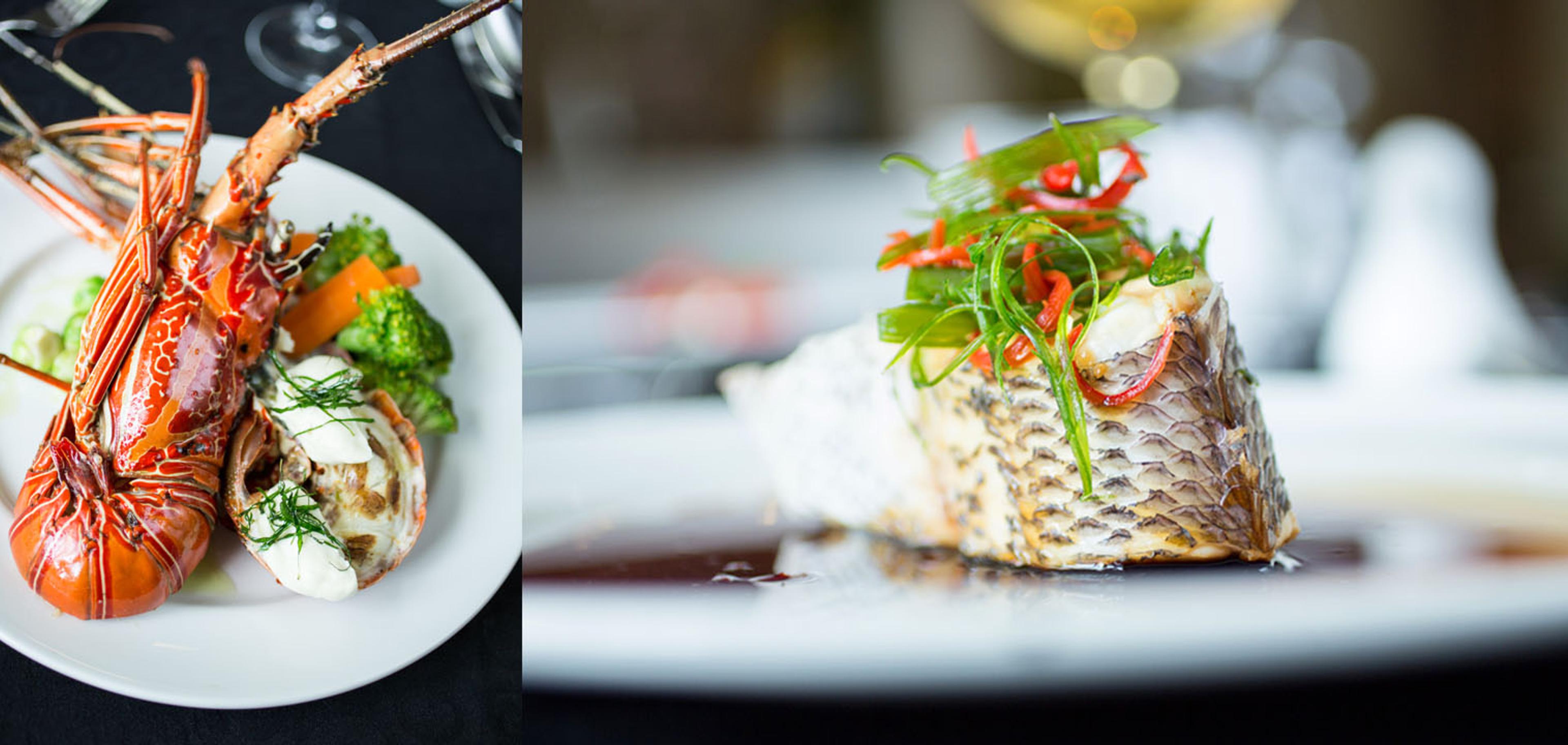 A plate of grilled lobster tail and vegetables beside a separate plate of a fish fillet topped with chilli and herbs.