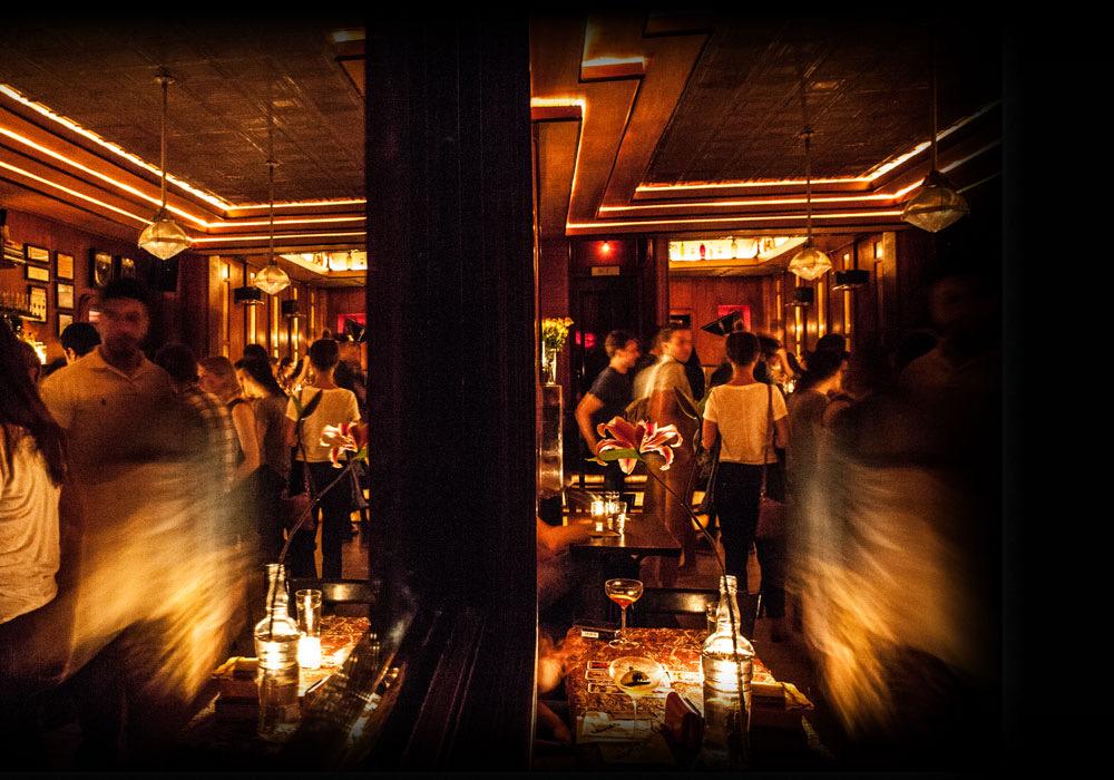 The bar at Employees Only at night, lit low and amber, with drinkers along the counter