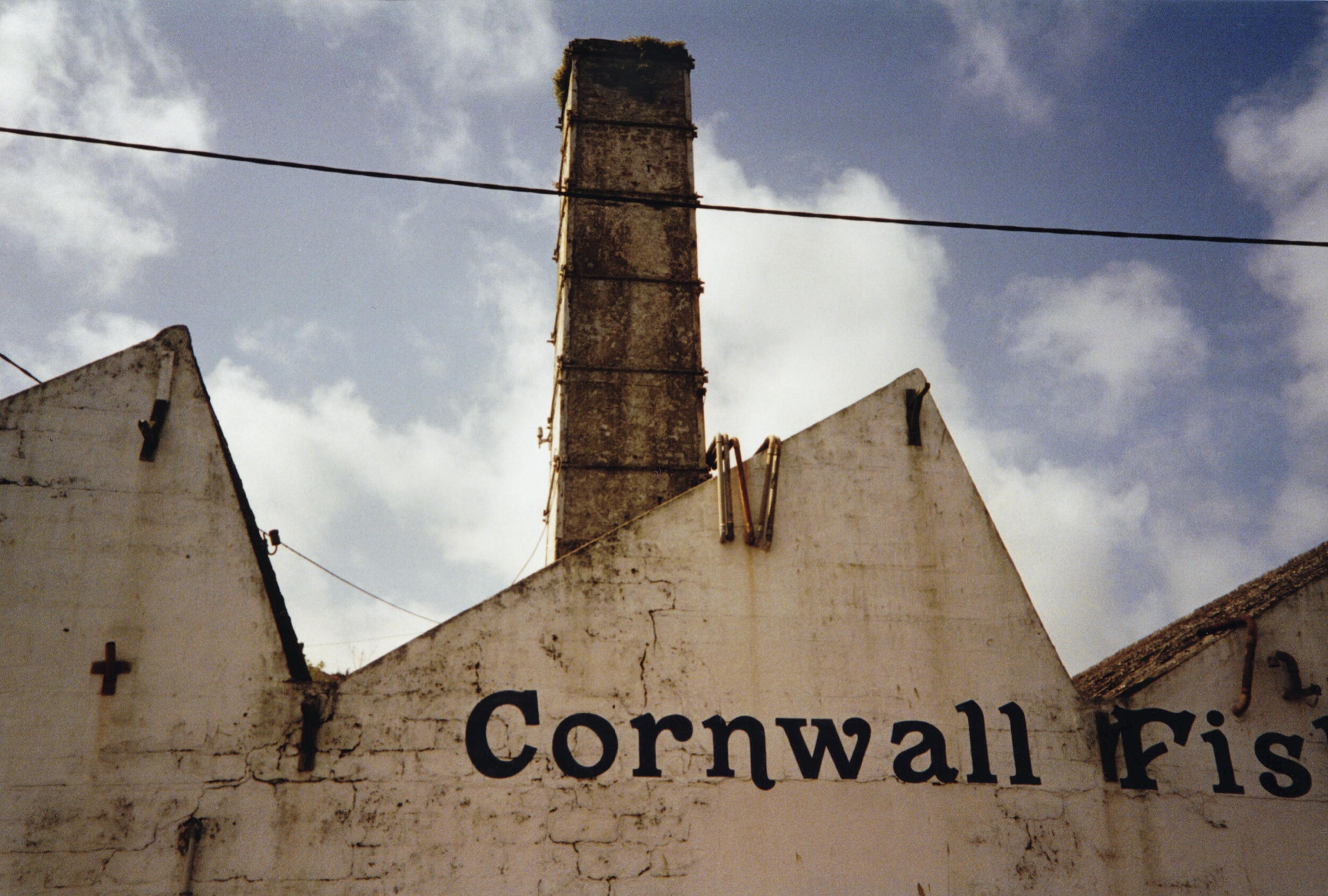 The old fish works on Newlyn harbour, its chimney and gable lettered Cornwall Fish, under a cloudy sky.