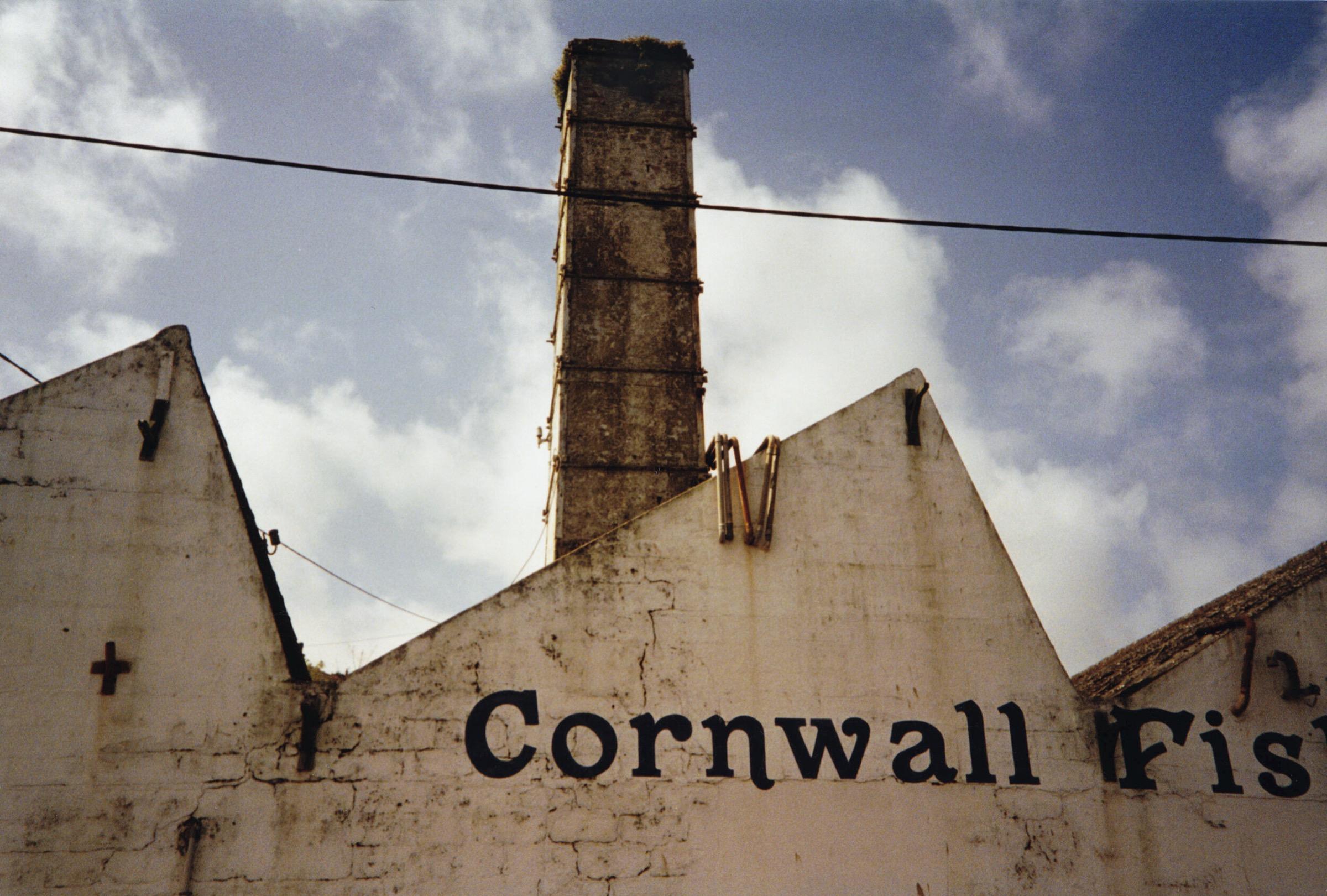 The old fish works on Newlyn harbour, its chimney and gable lettered Cornwall Fish, under a cloudy sky.