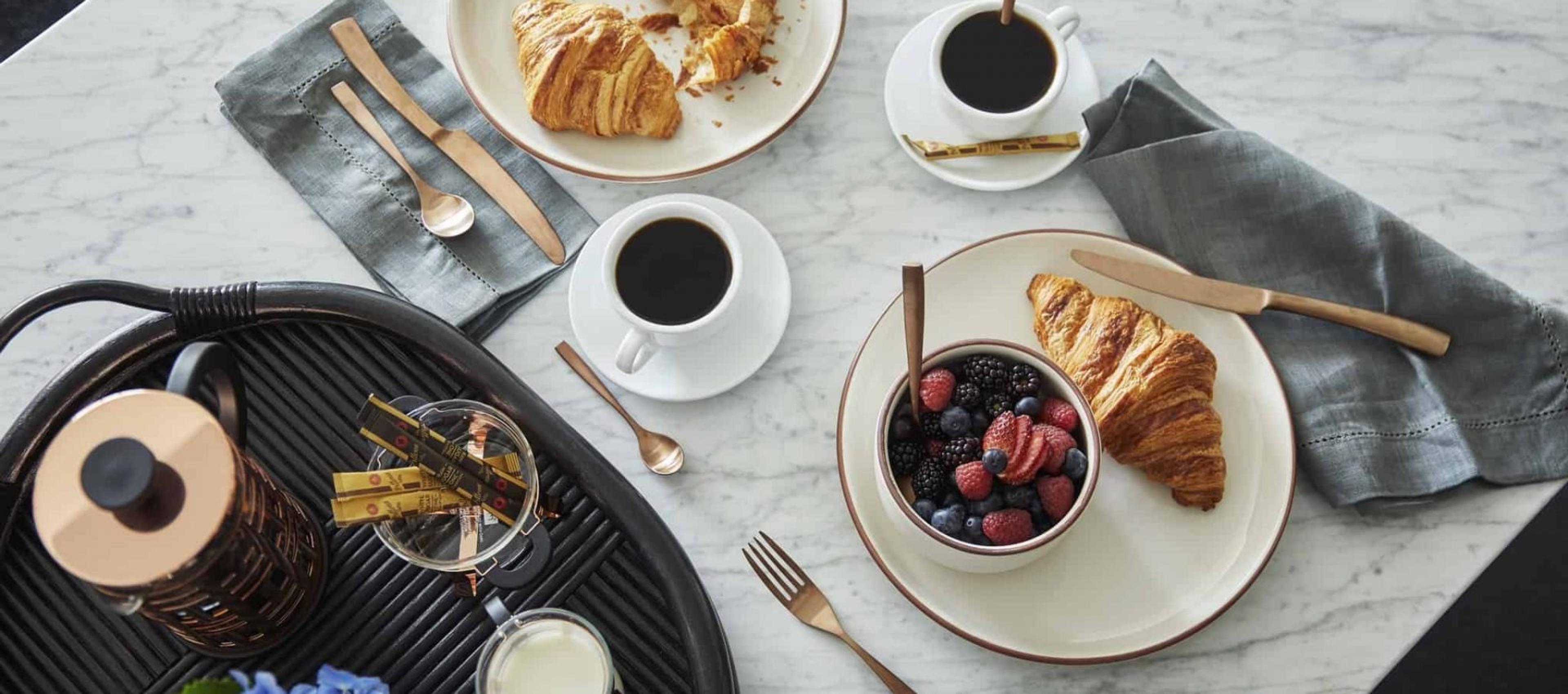 A marble table set with croissants, coffee, and a bowl of mixed berries, seen from above.