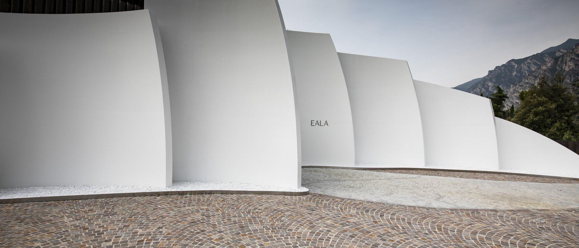 the curved white concrete entrance facade of the hotel, with its name set into the wall, at the base of a mountain