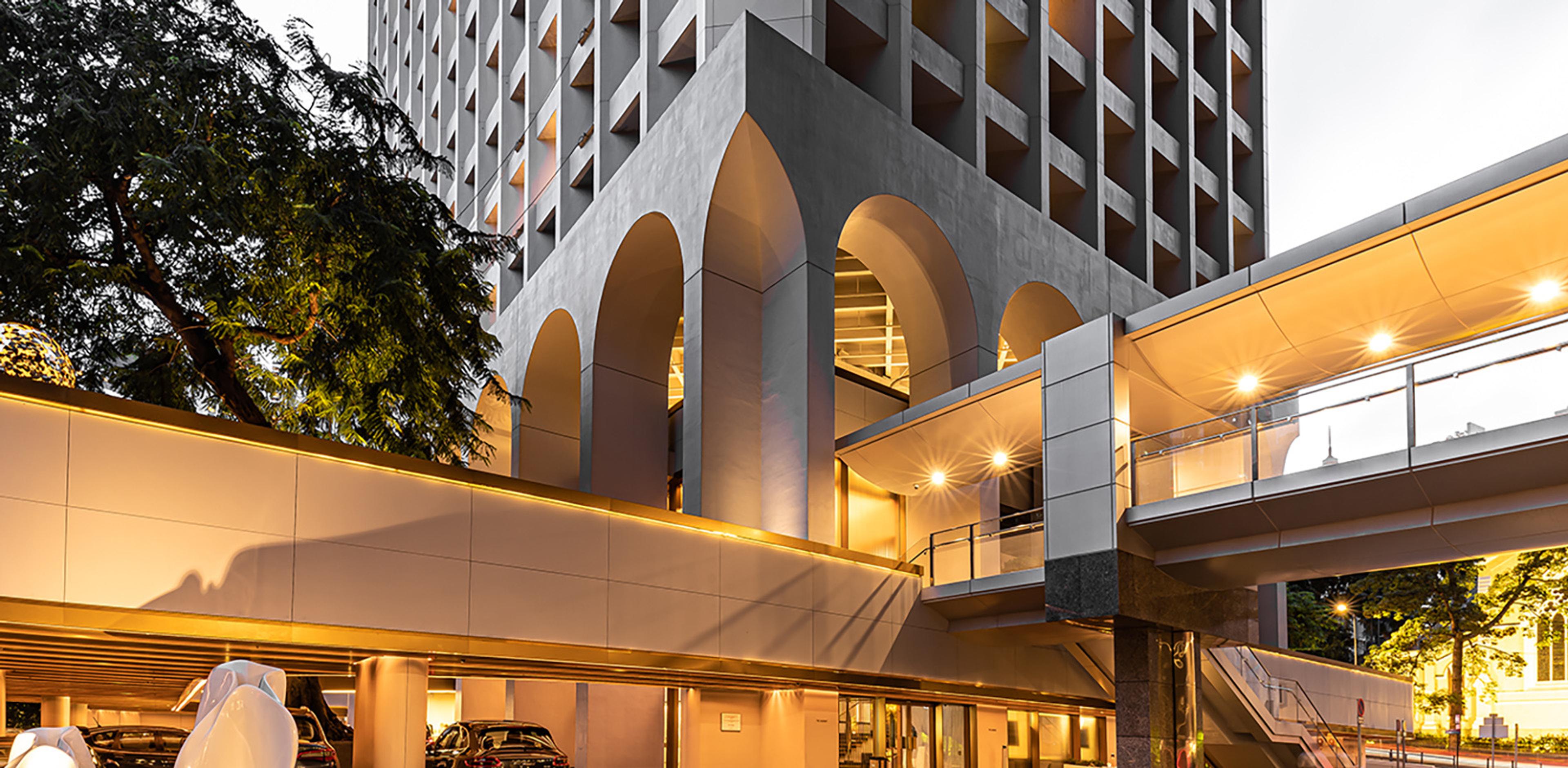 the hotel's arched concrete facade lit at dusk above a covered driveway and a glass walkway