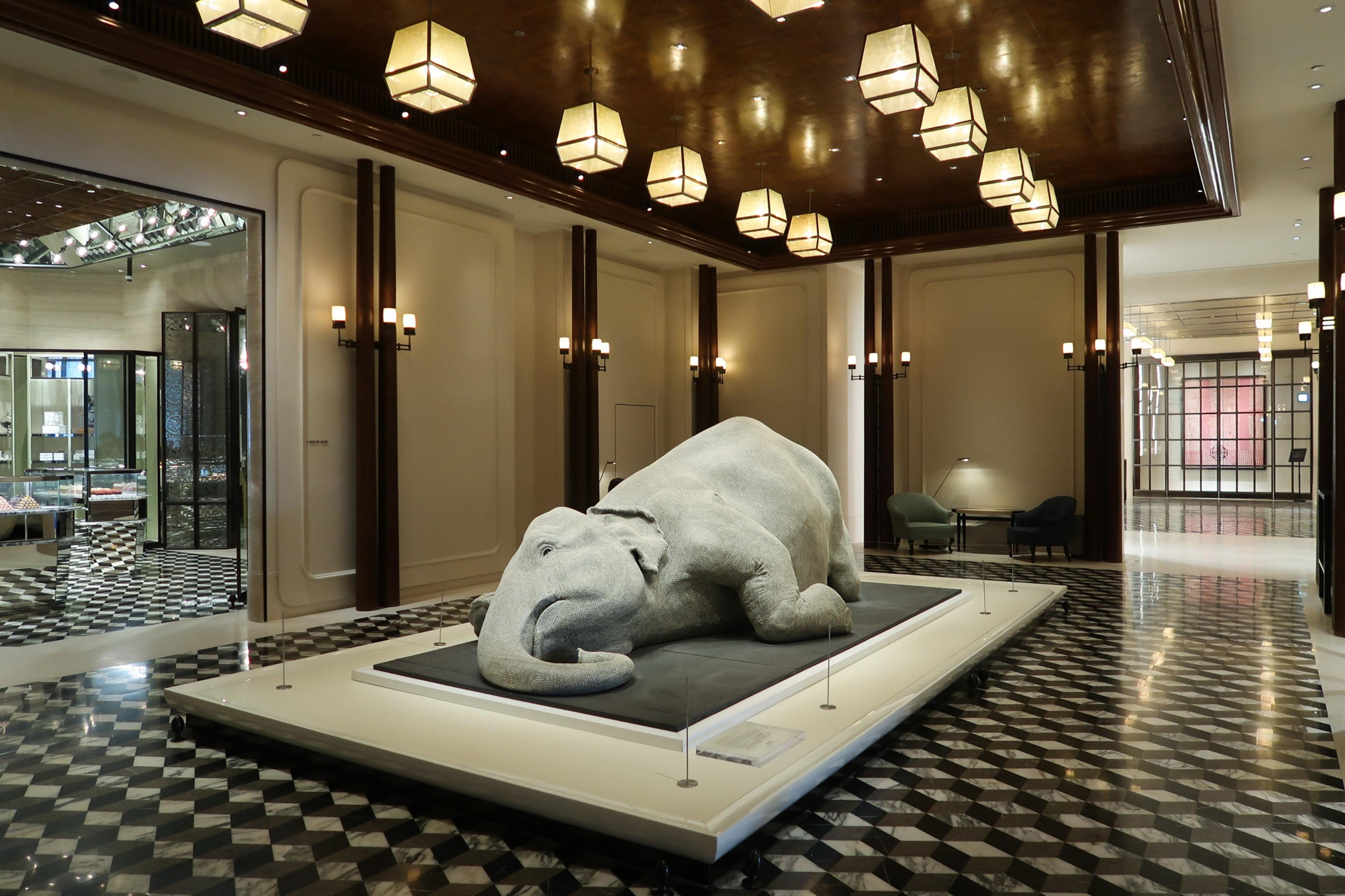 A lobby with a large stone elephant sculpture under clusters of lantern lights