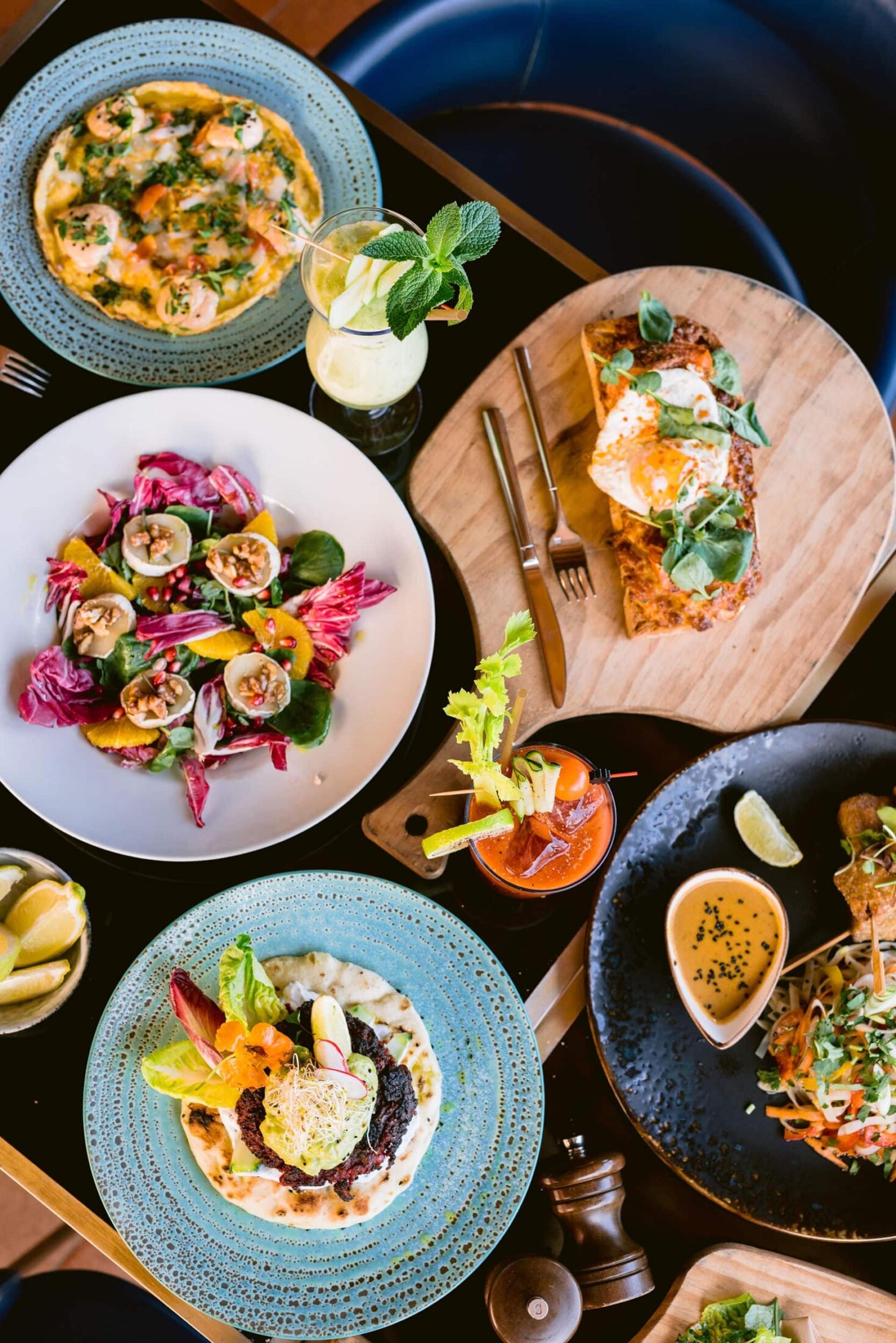 Plates of salad, eggs, prawns and a Bloody Mary on a dark table, seen from above