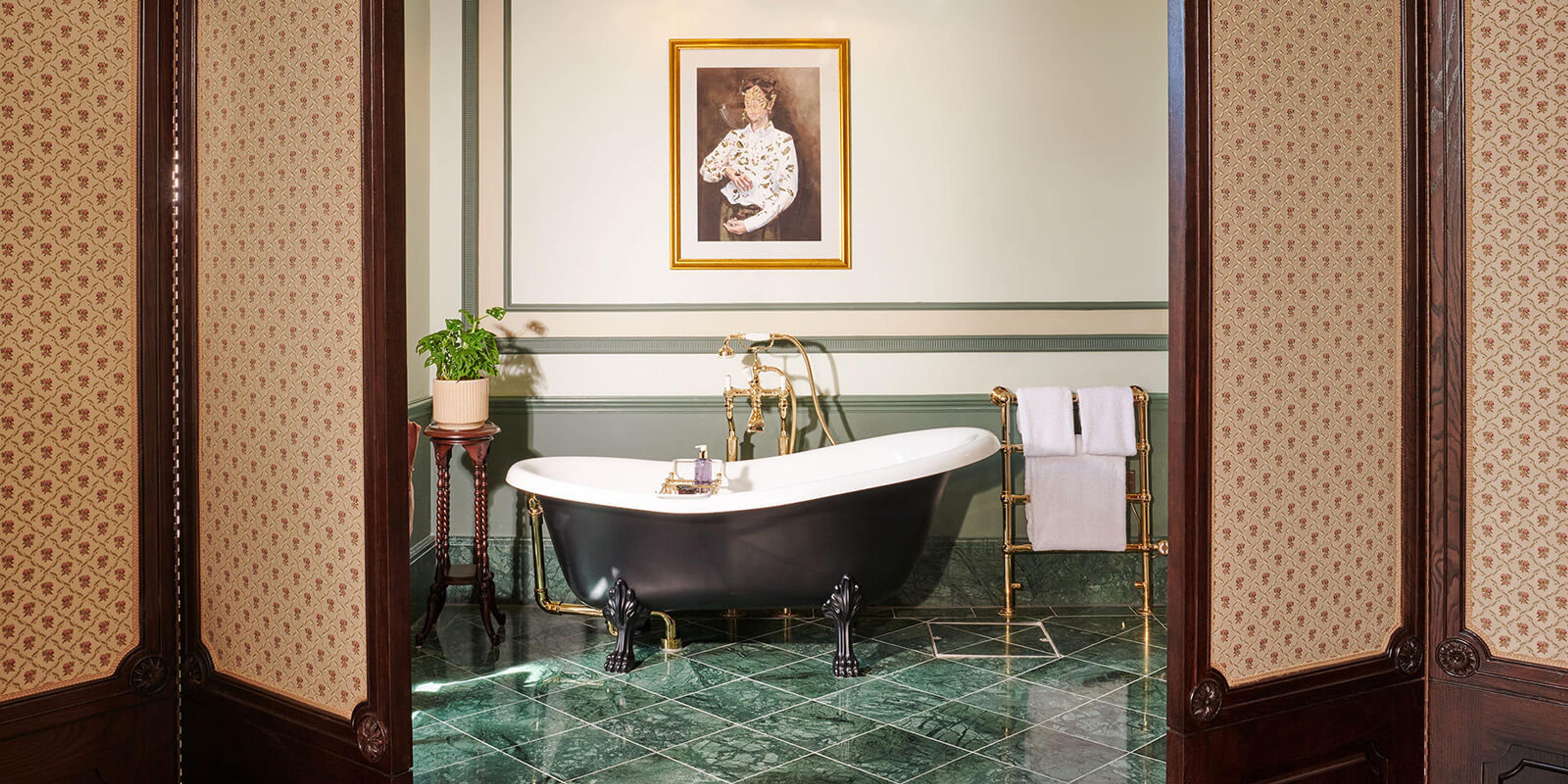 a black roll top bath on clawed feet in a room with green marble floor tiles and a framed portrait on the wall