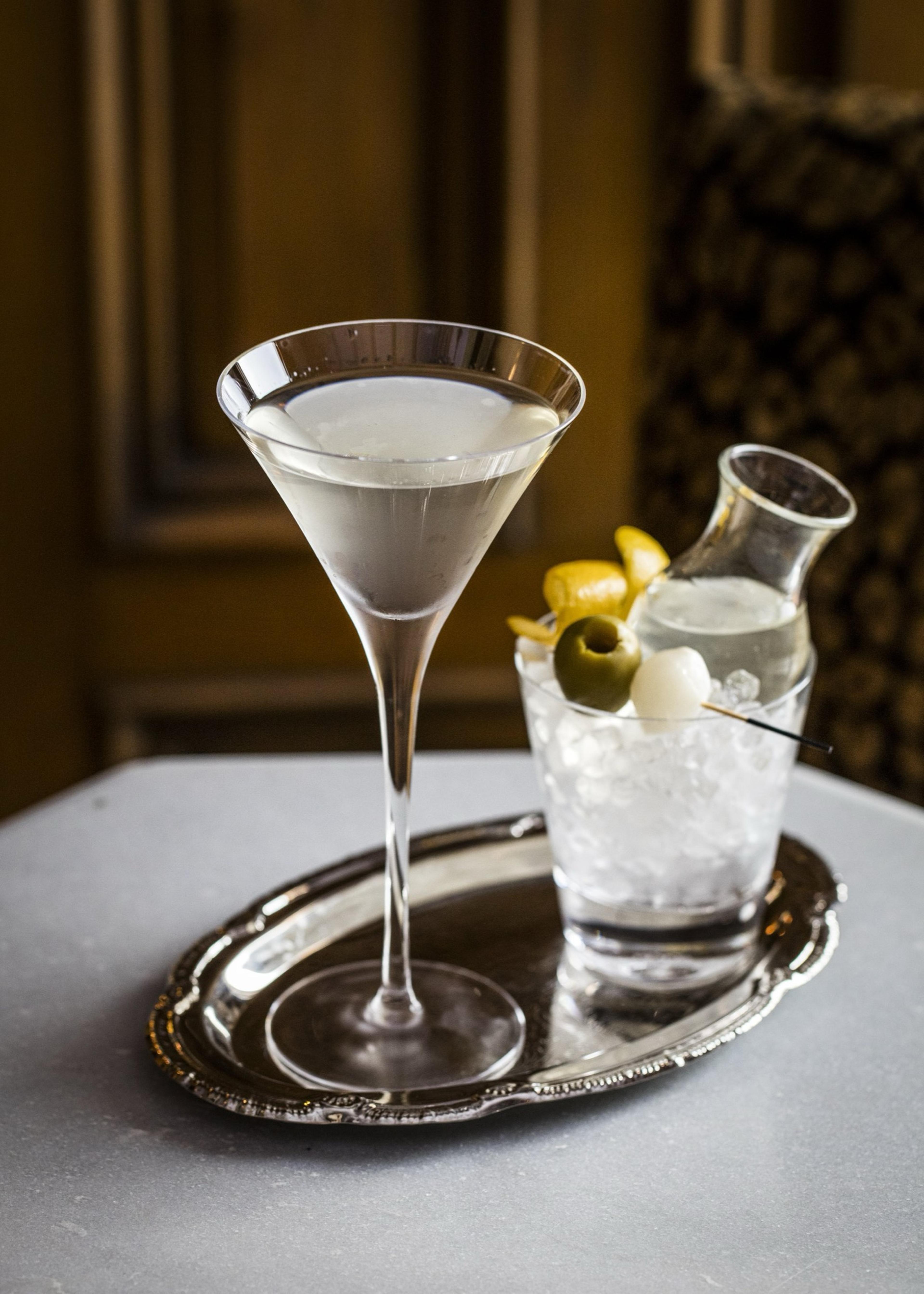 A martini in a long stemmed glass beside a rocks glass with ice, olives, and a lemon twist, set on a silver tray.