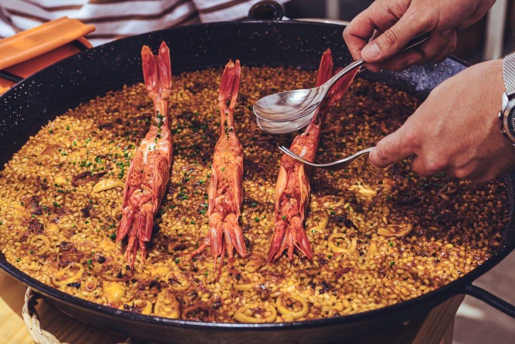 A pan of rice topped with red prawns, served at the table
