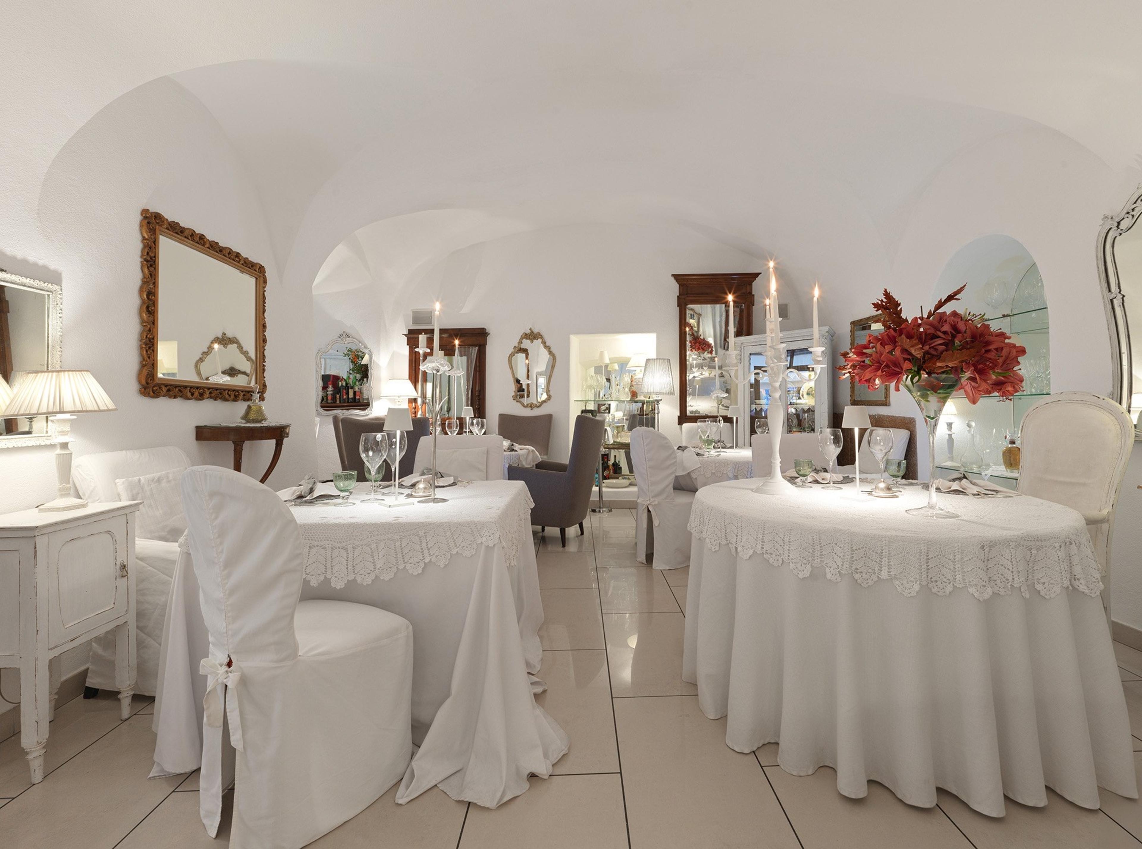 A vaulted dining room with white tablecloths and red flowers on the tables