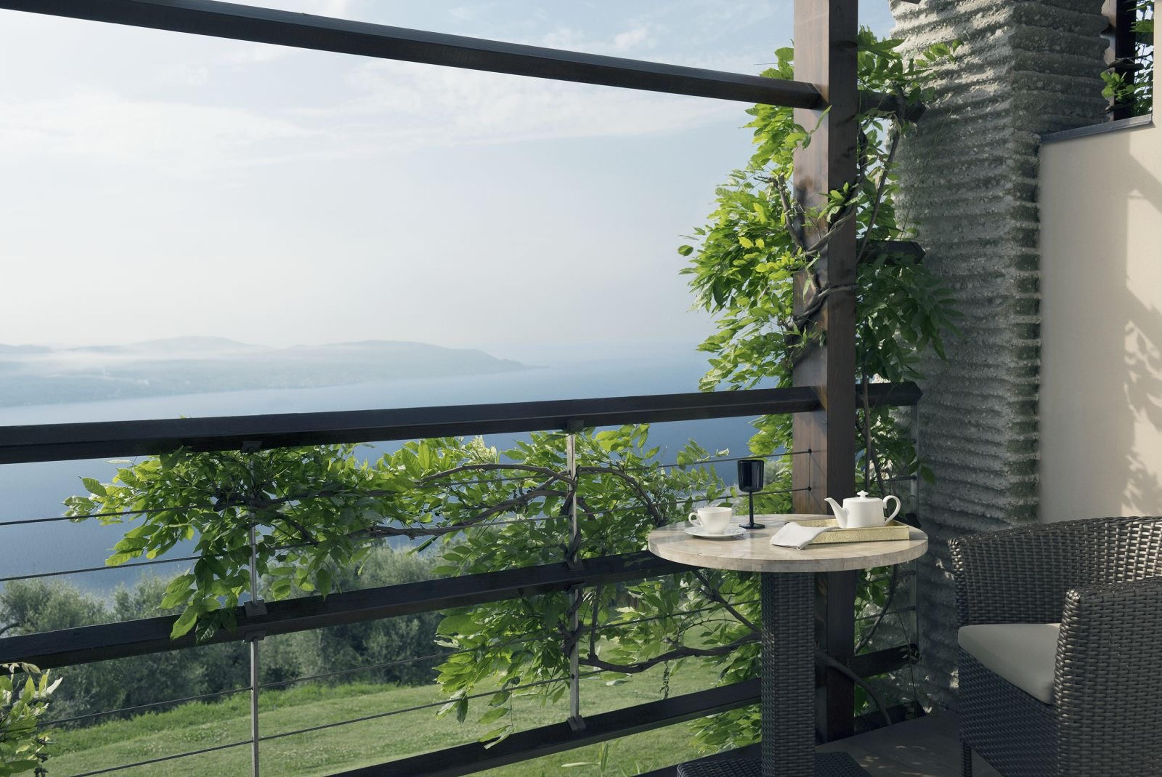 A small balcony table set with tea things, seen through a timber railing hung with vines, with the lake below.