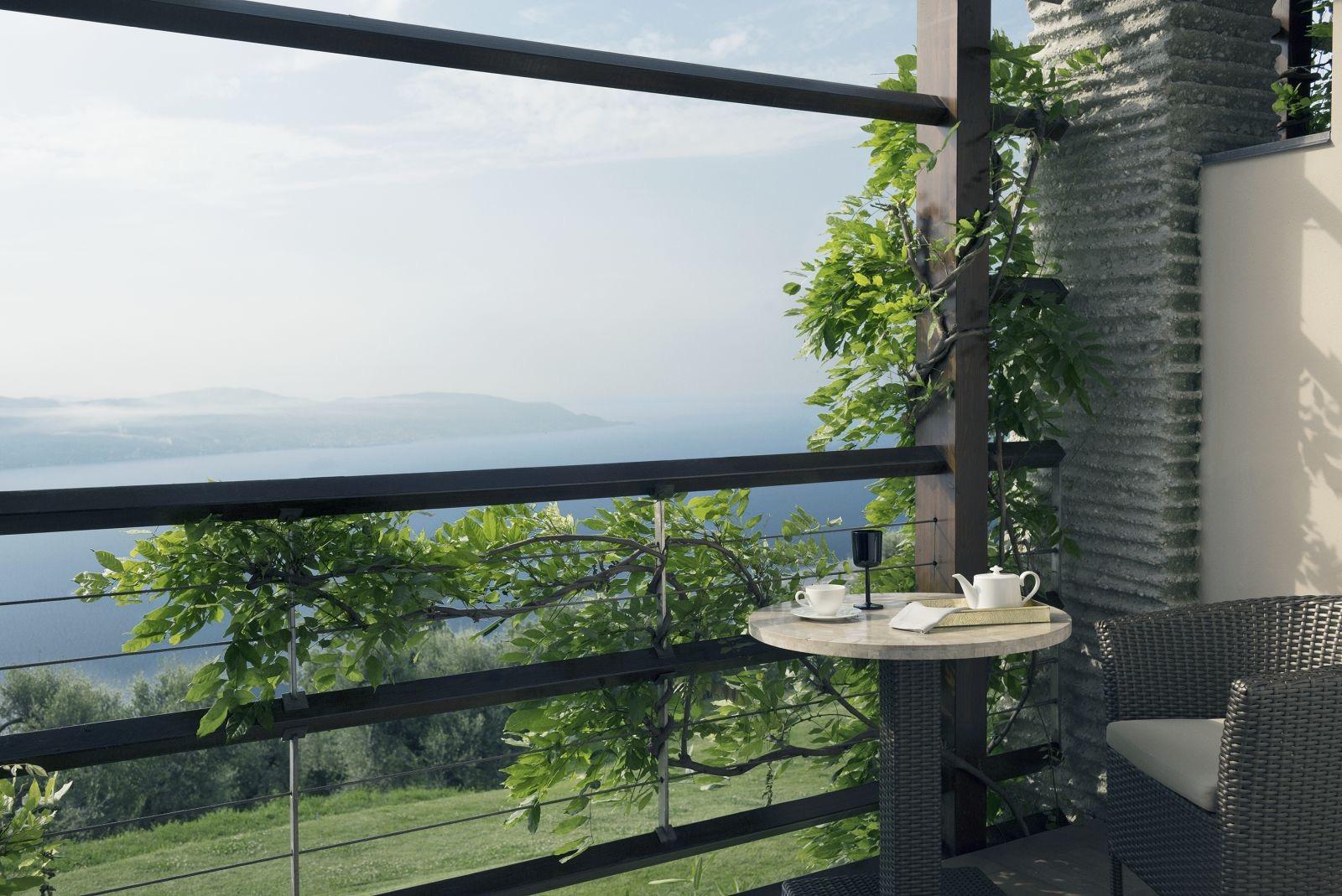 A small balcony table set with tea things, seen through a timber railing hung with vines, with the lake below.