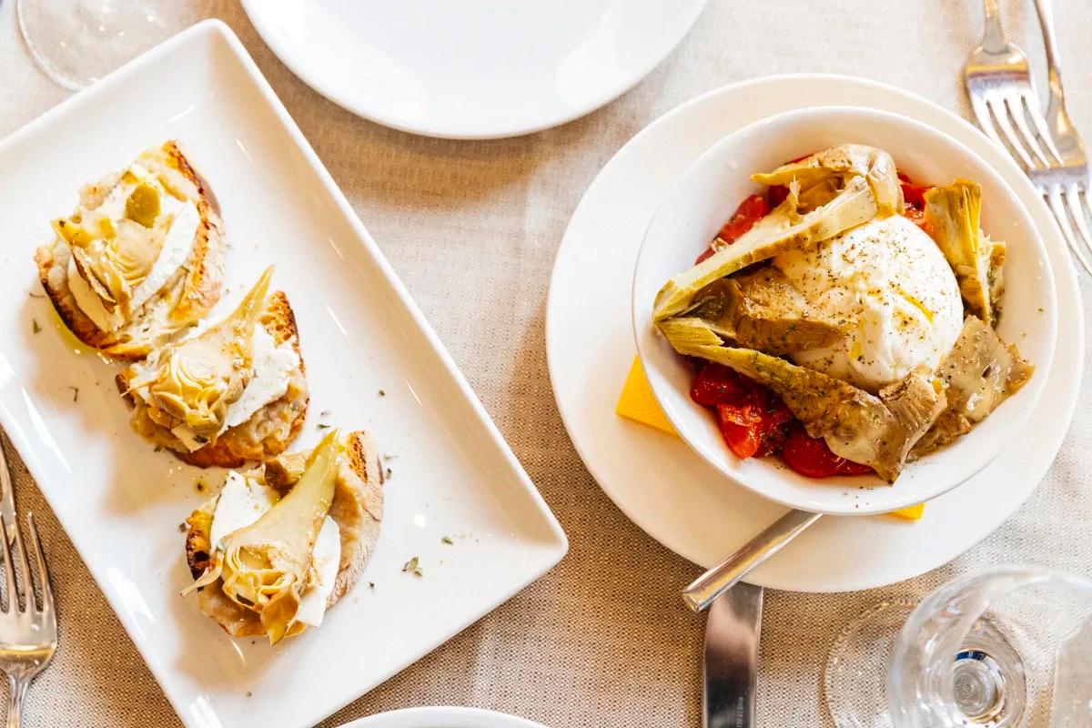 Plates of fried courgette flowers and pasta on a white tablecloth
