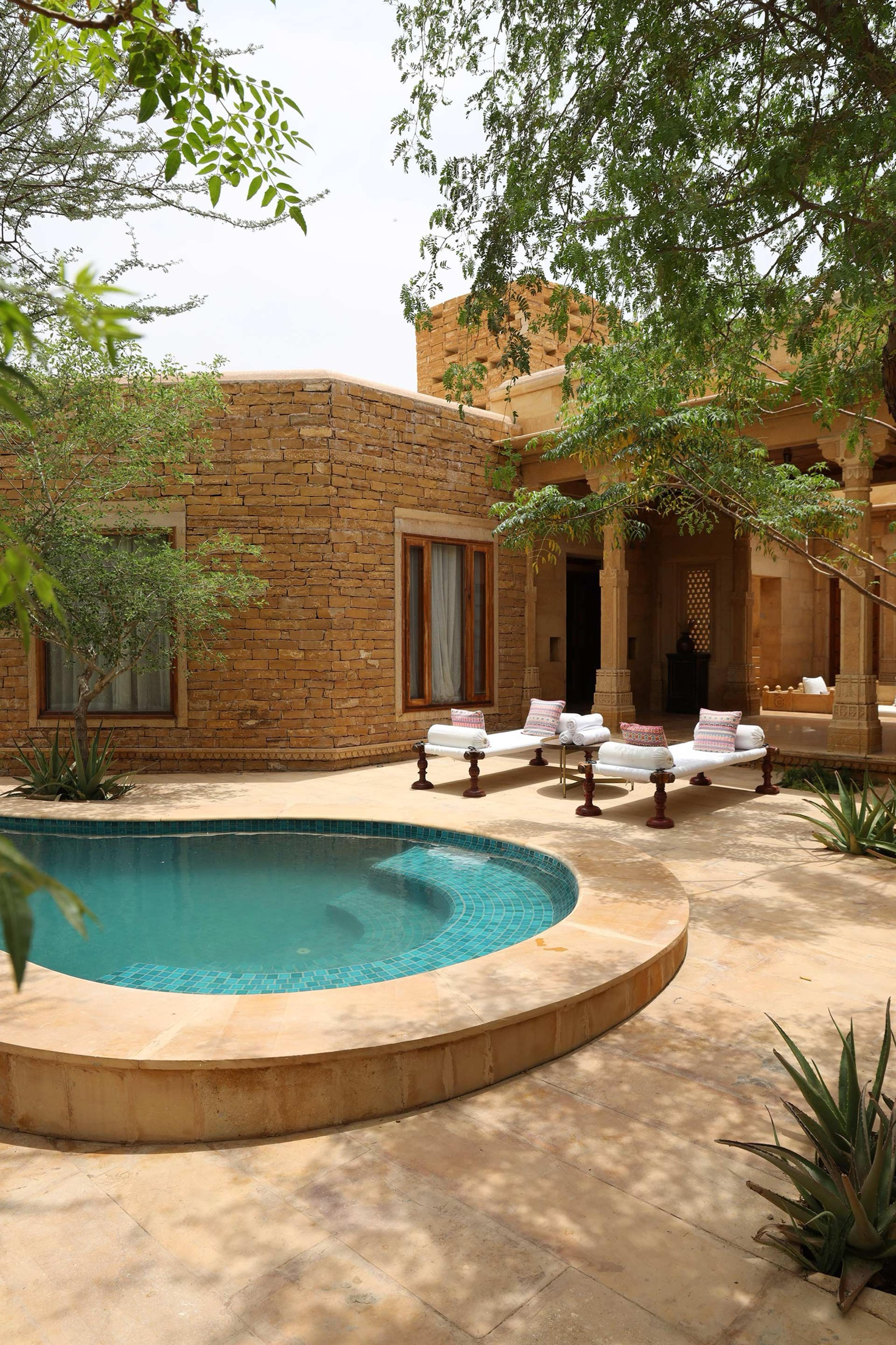 a round plunge pool on a sandstone terrace, with two loungers and the hotel's turreted facade behind