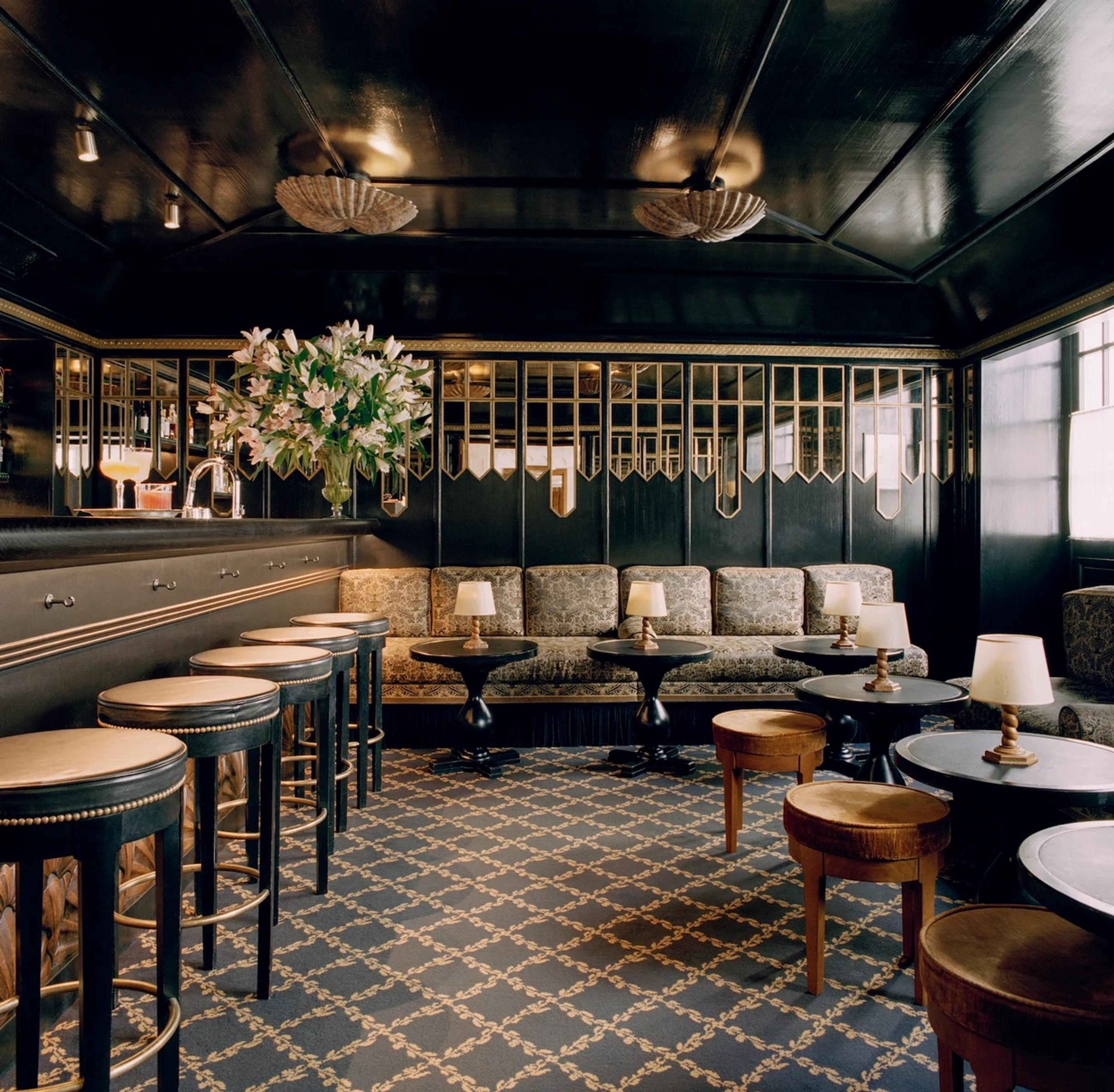 A dark green bar with brass stools around a curved counter and low armchairs on a patterned floor.