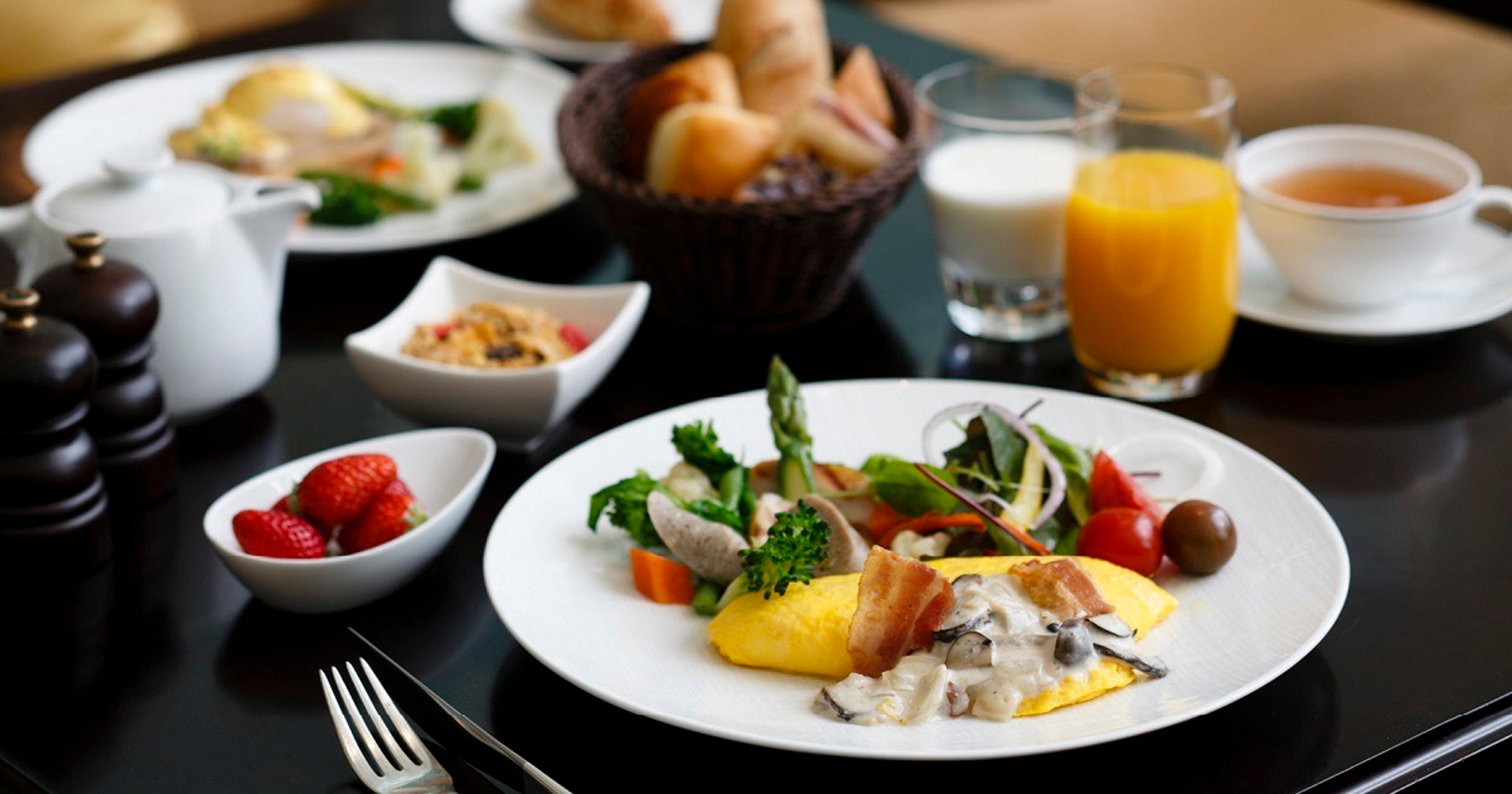 A table set for breakfast with a plate of omelette, bacon and vegetables, a bowl of strawberries, a bread basket, and glasses of juice and milk.