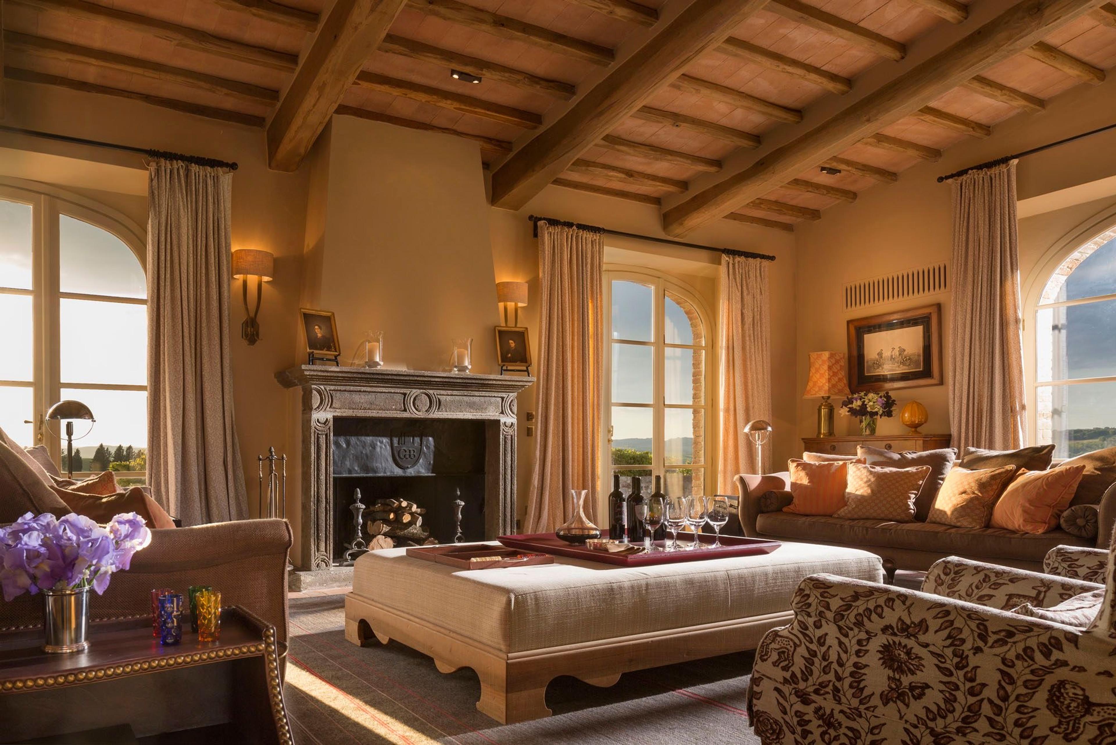 A sitting room with exposed wood beams, a stone fireplace, armchairs and a sofa, and a low table set with glasses and a decanter.