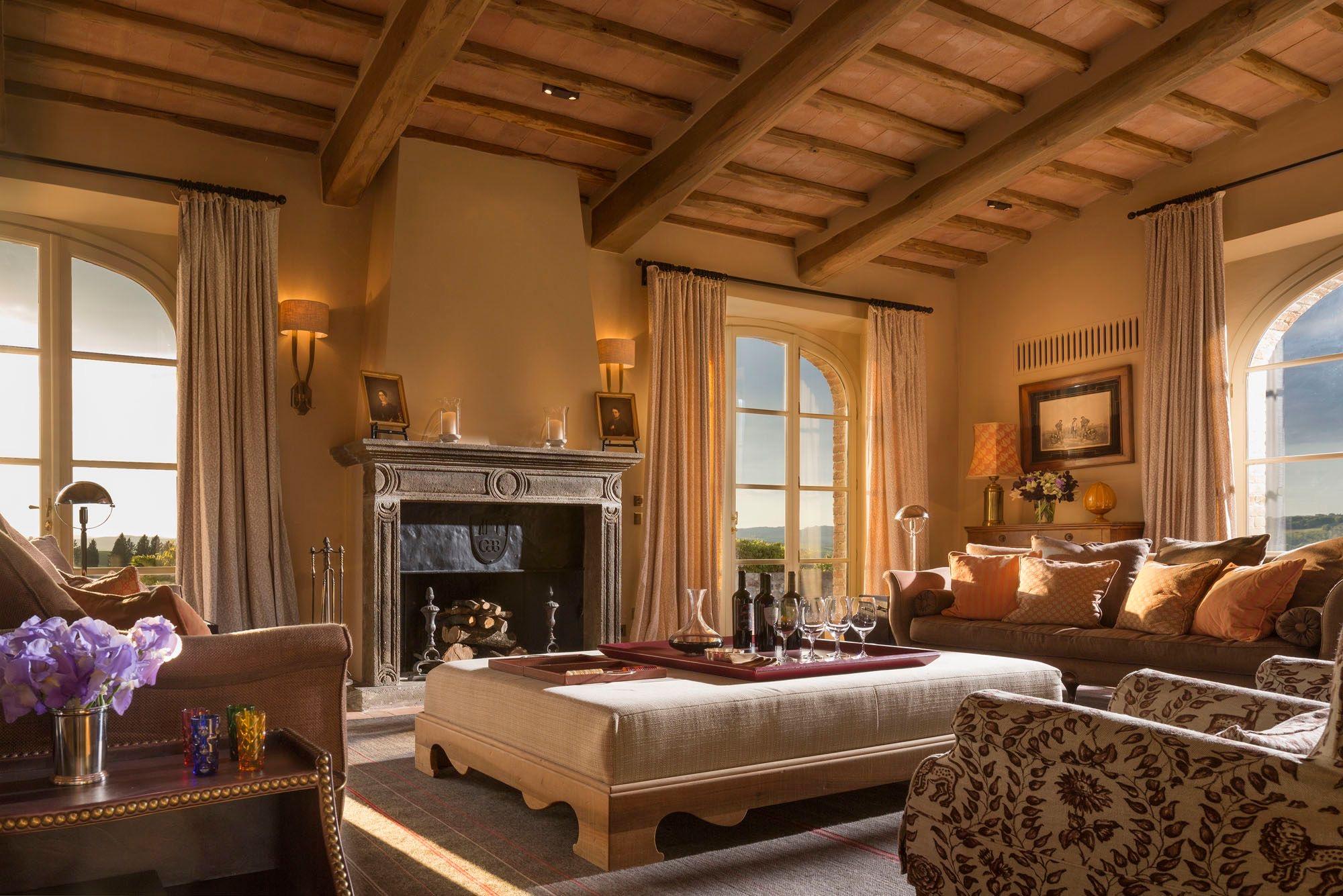 A sitting room with exposed wood beams, a stone fireplace, armchairs and a sofa, and a low table set with glasses and a decanter.