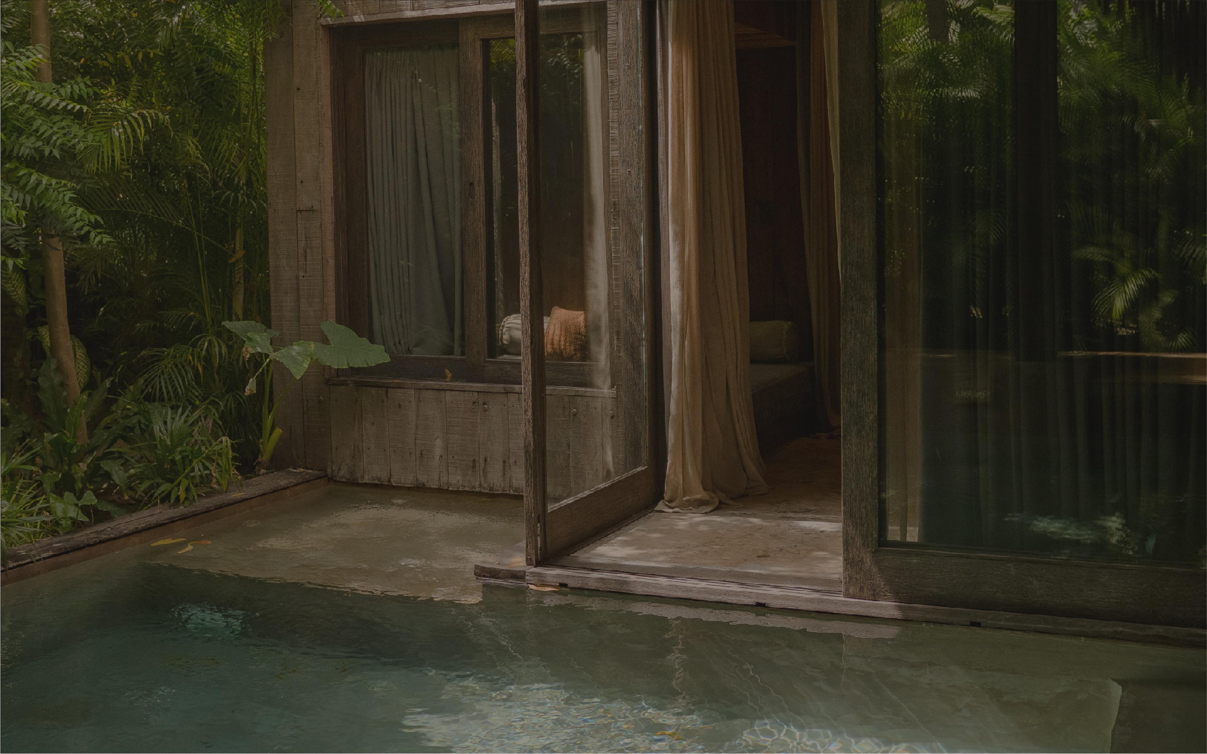 A villa's open doors beside a plunge pool, surrounded by jungle.