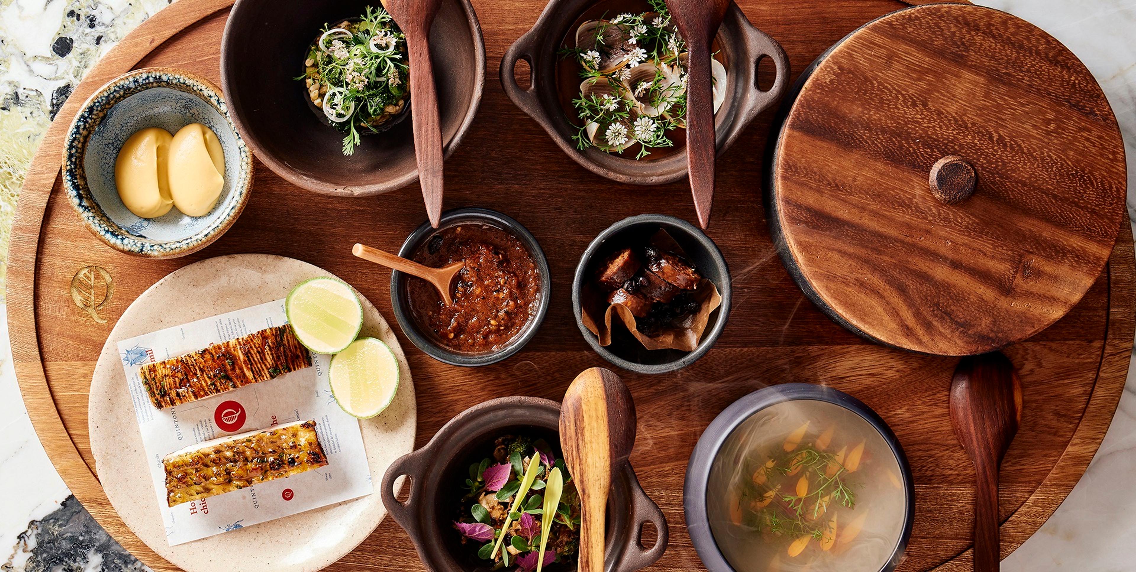 Dishes from Quintonil's menu laid out on a dark wooden table, seen from above