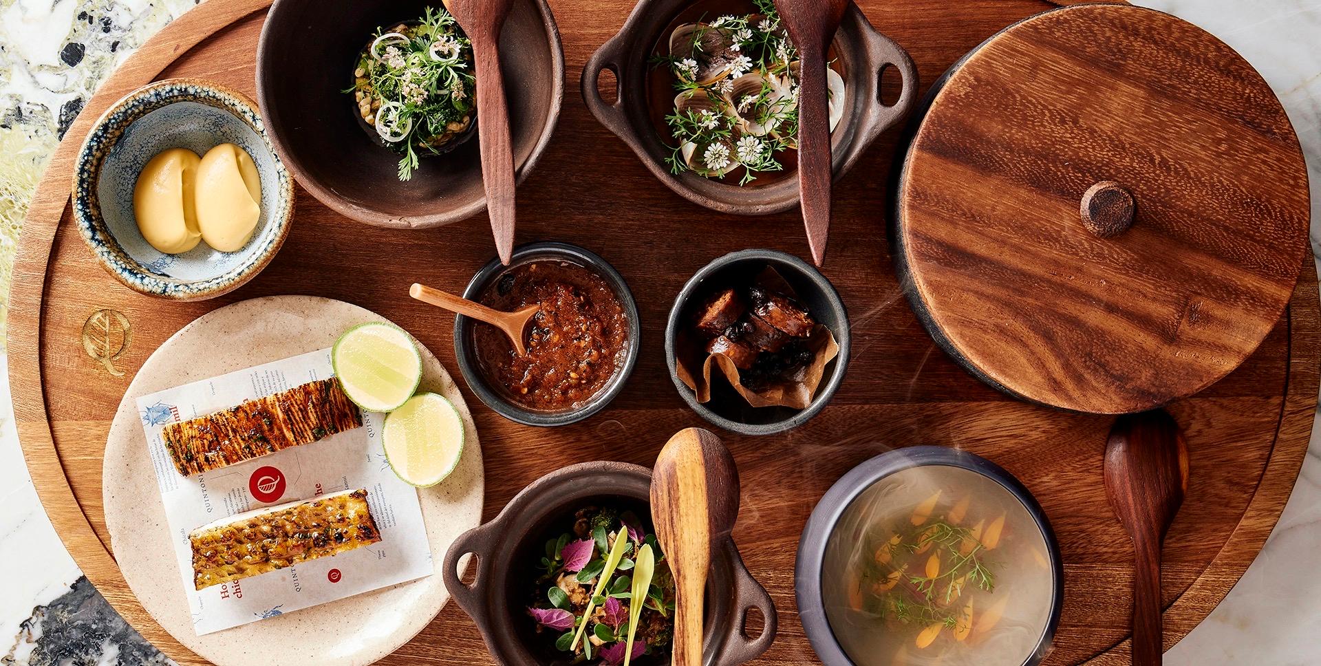 Dishes from Quintonil's menu laid out on a dark wooden table, seen from above