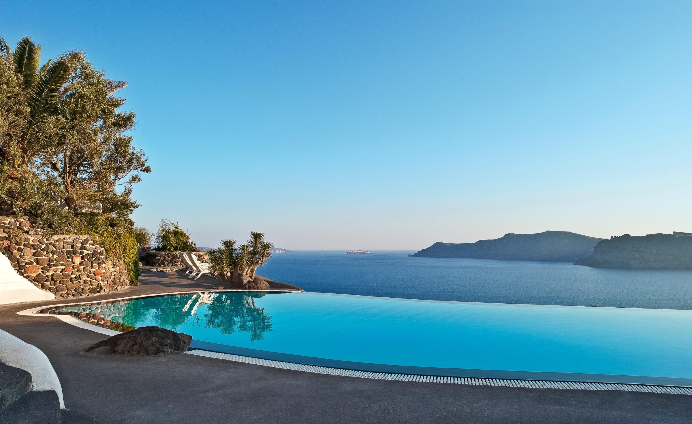 An infinity pool edged by palm trees, its water meeting the sea with a distant headland on the horizon.