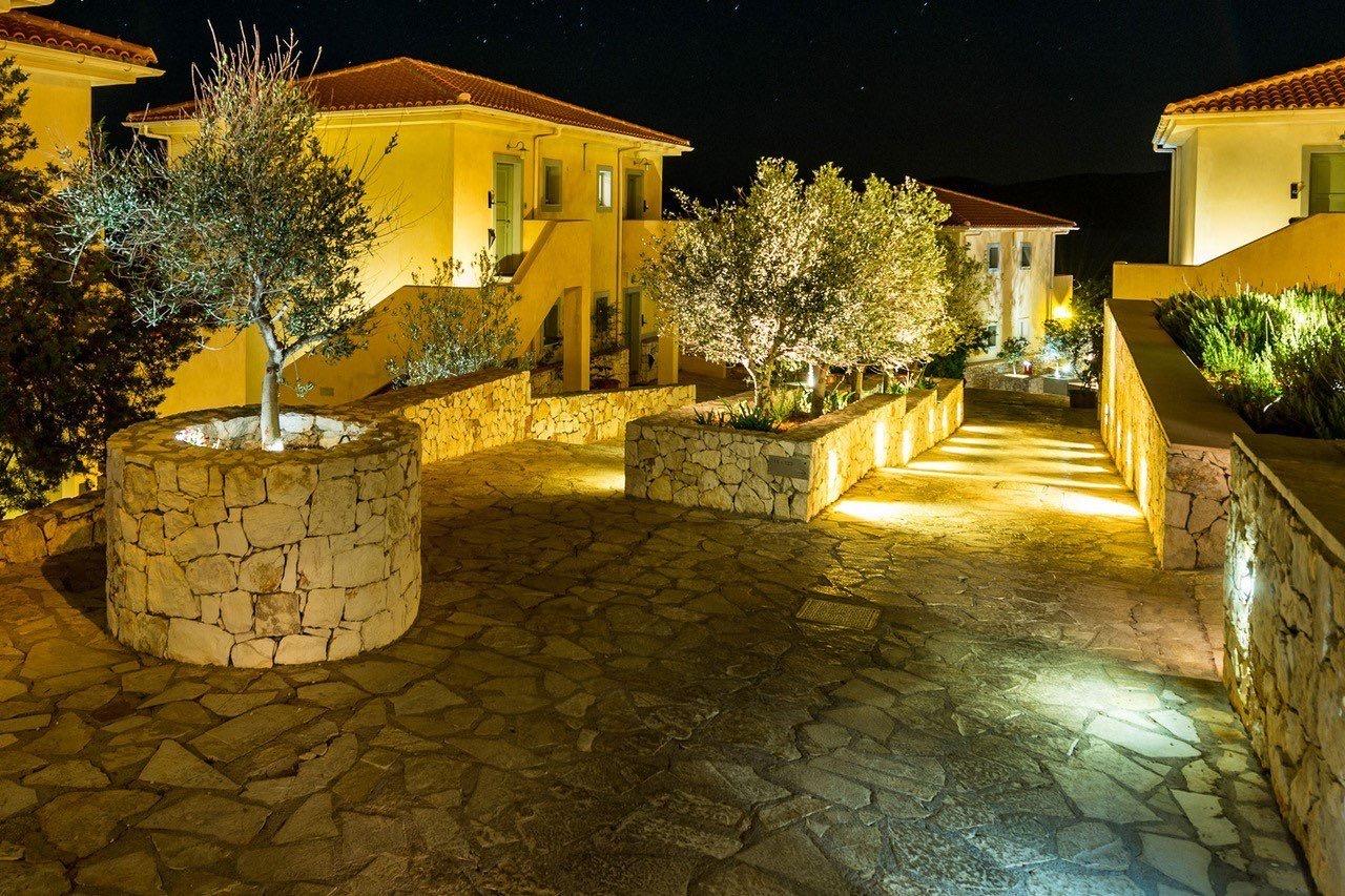 A stone courtyard at night, lit pathways and an olive tree between the resort's terracotta-roofed buildings.