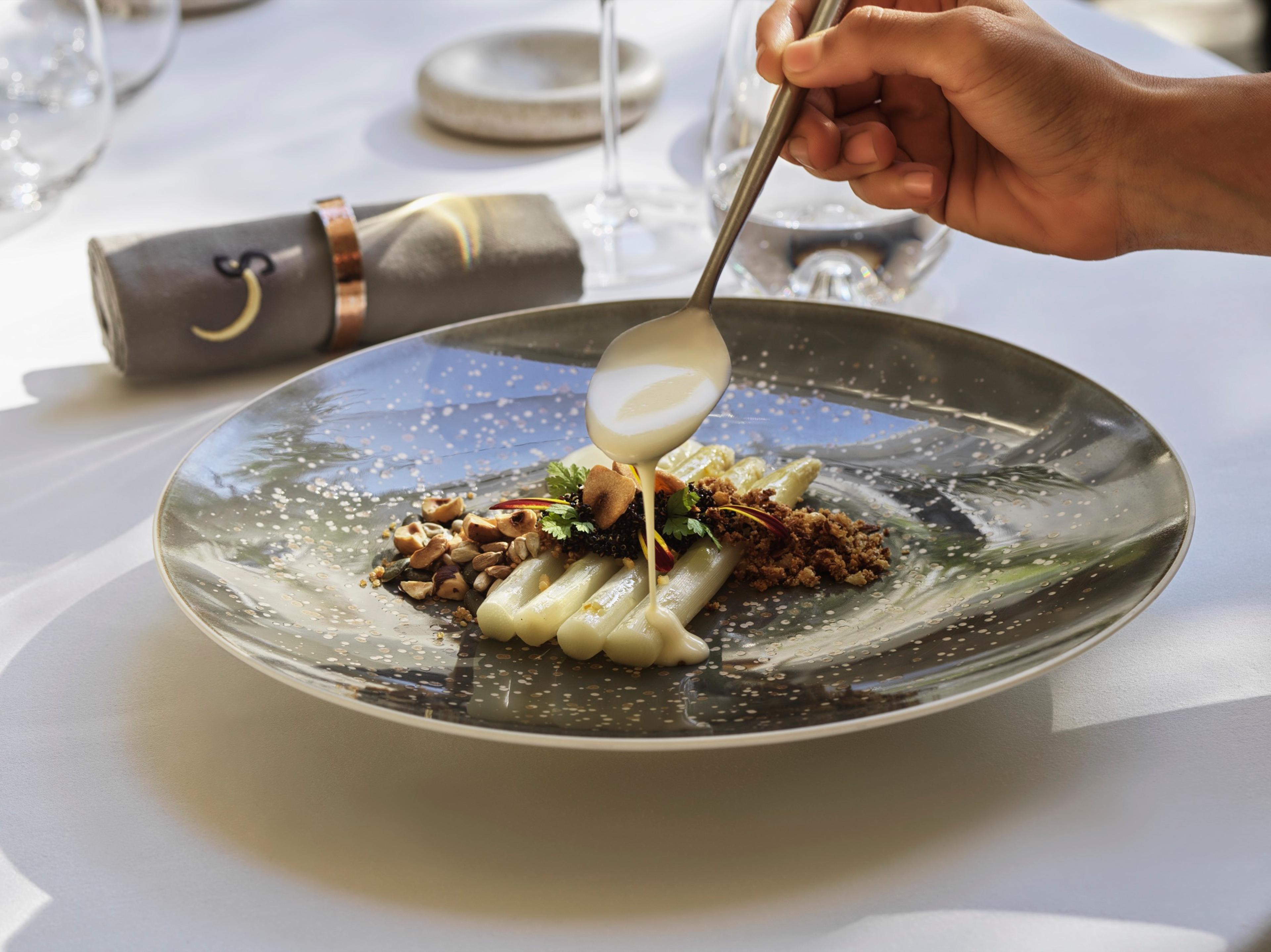 A plated dish being finished with a spoonful of sauce
