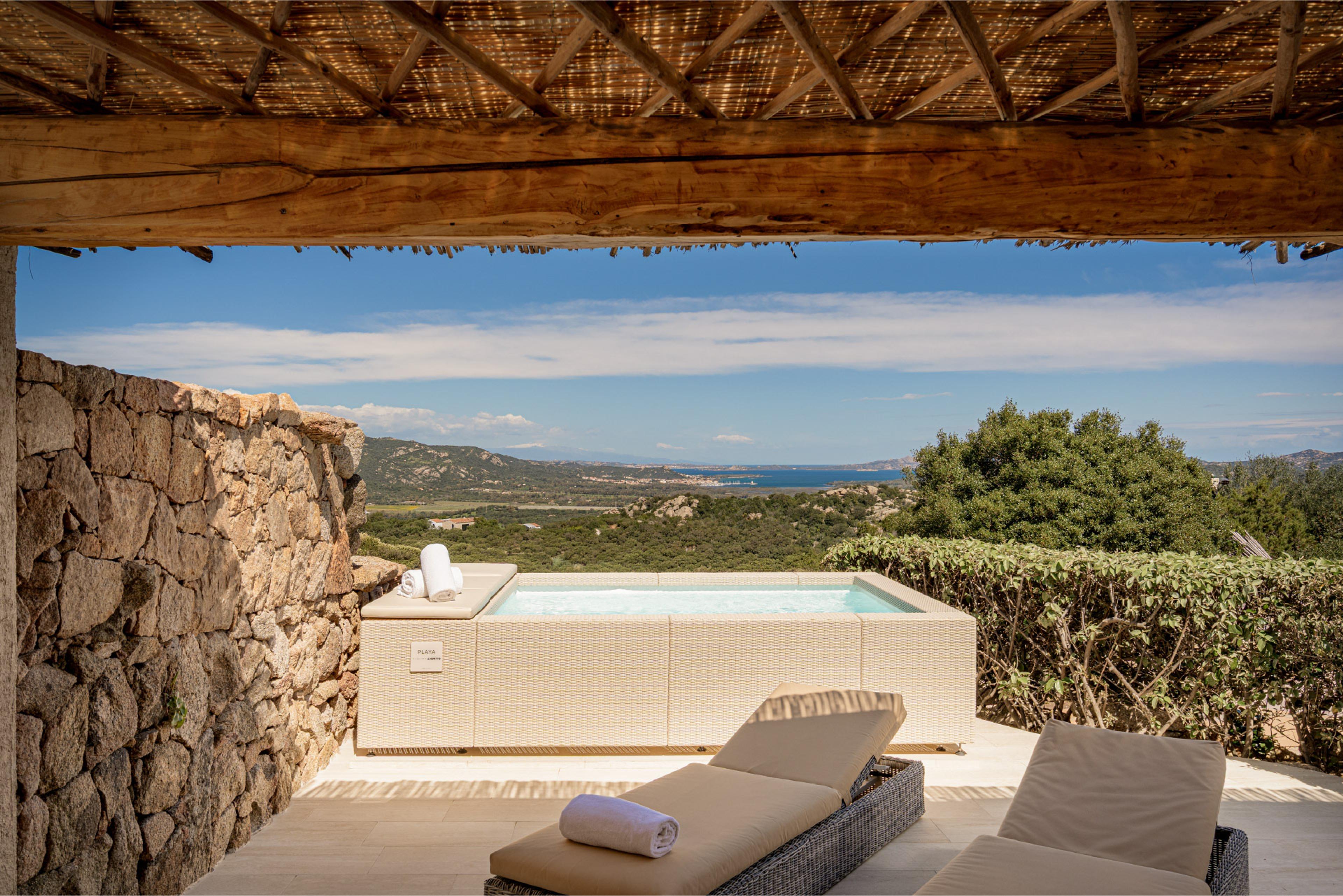A terrace under a timber and reed roof, with a plunge pool and sun loungers, looking out over a wide view of hills and sea.