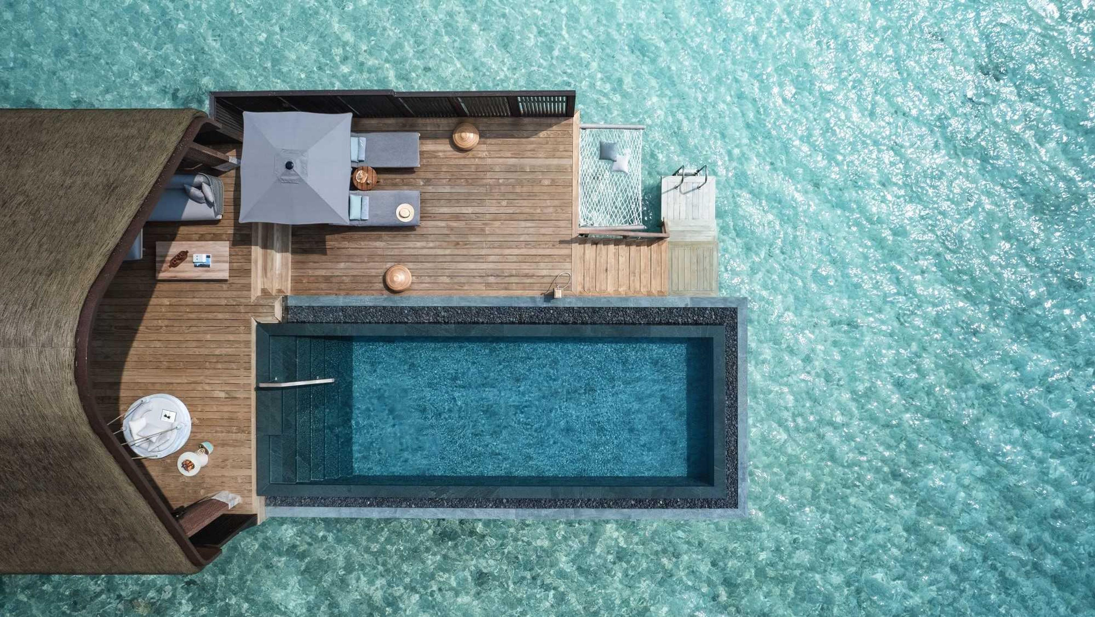 An over-water villa seen from directly above, its long pool and deck set in turquoise water.