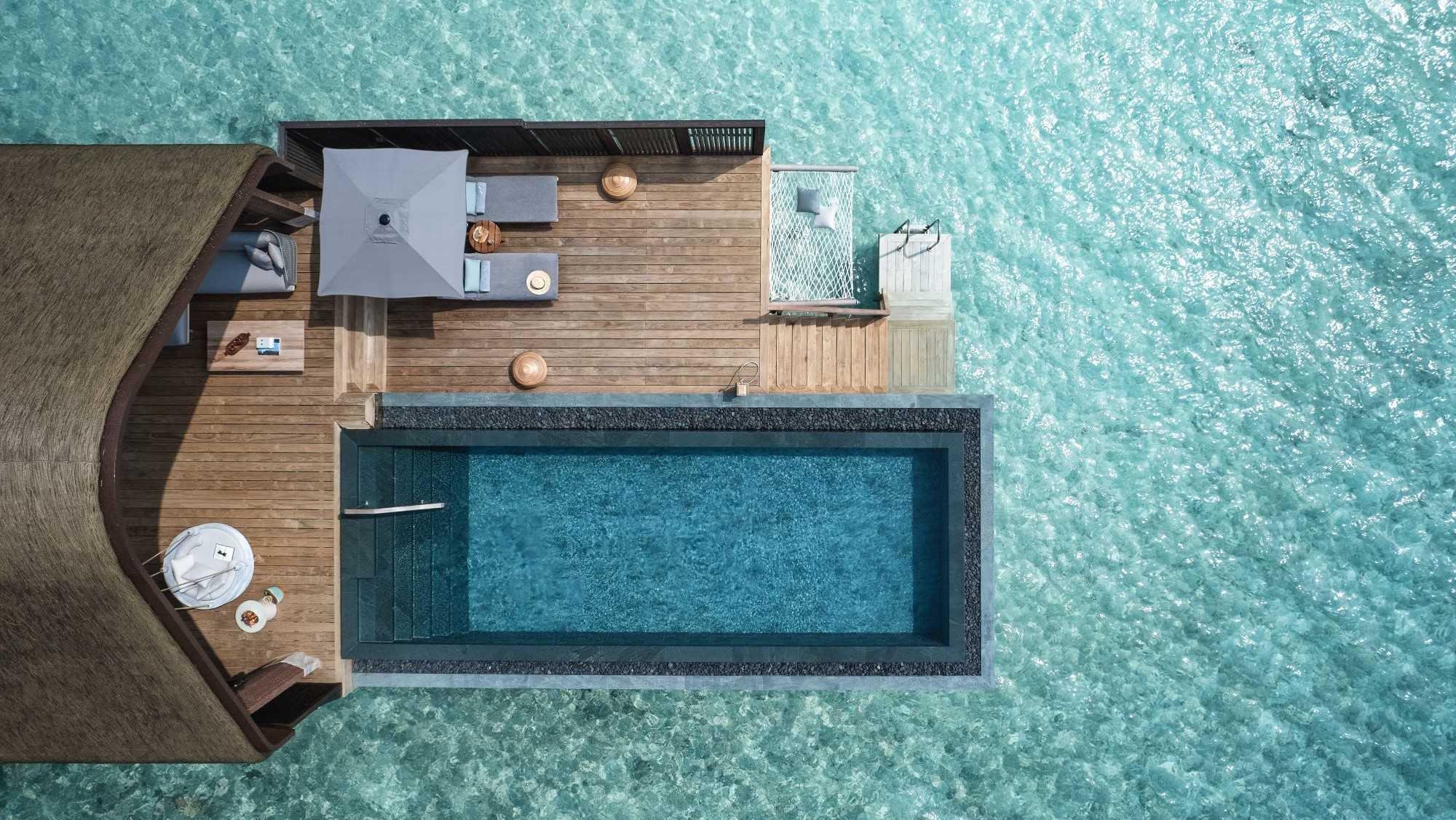 An over-water villa seen from directly above, its long pool and deck set in turquoise water.