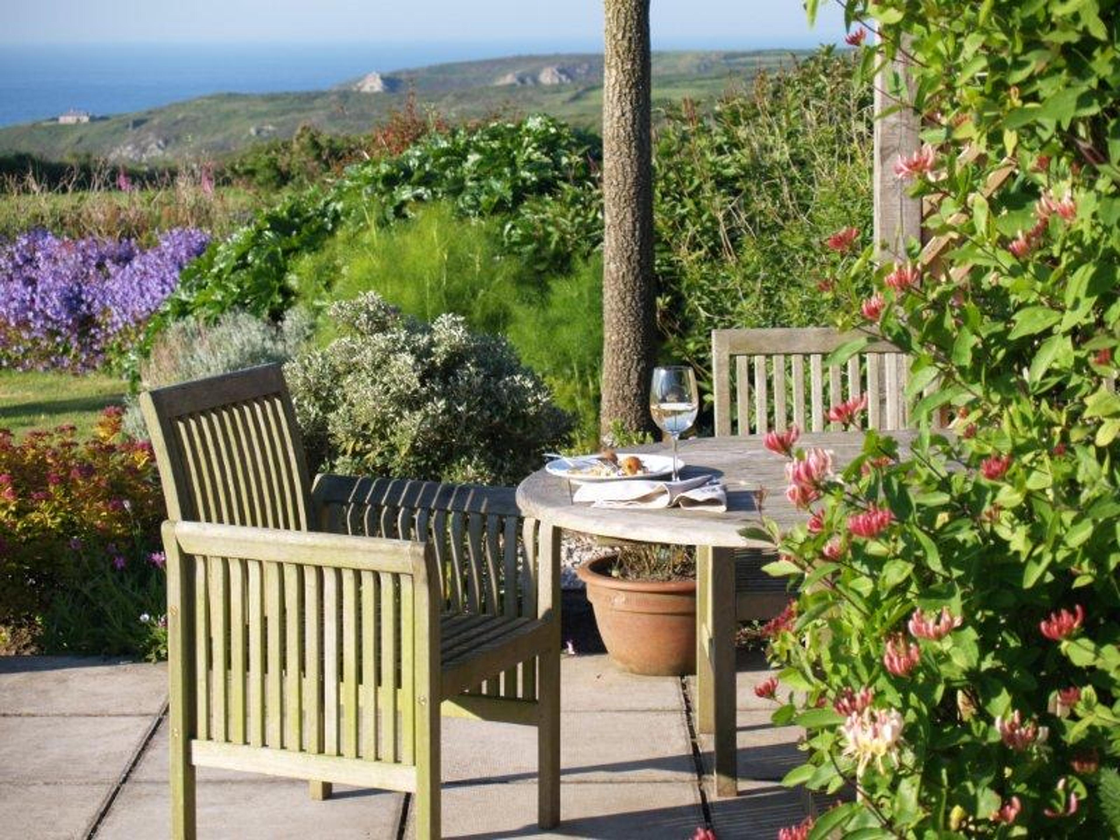A table and two wooden chairs in a flowering garden, with the moor and the sea beyond.