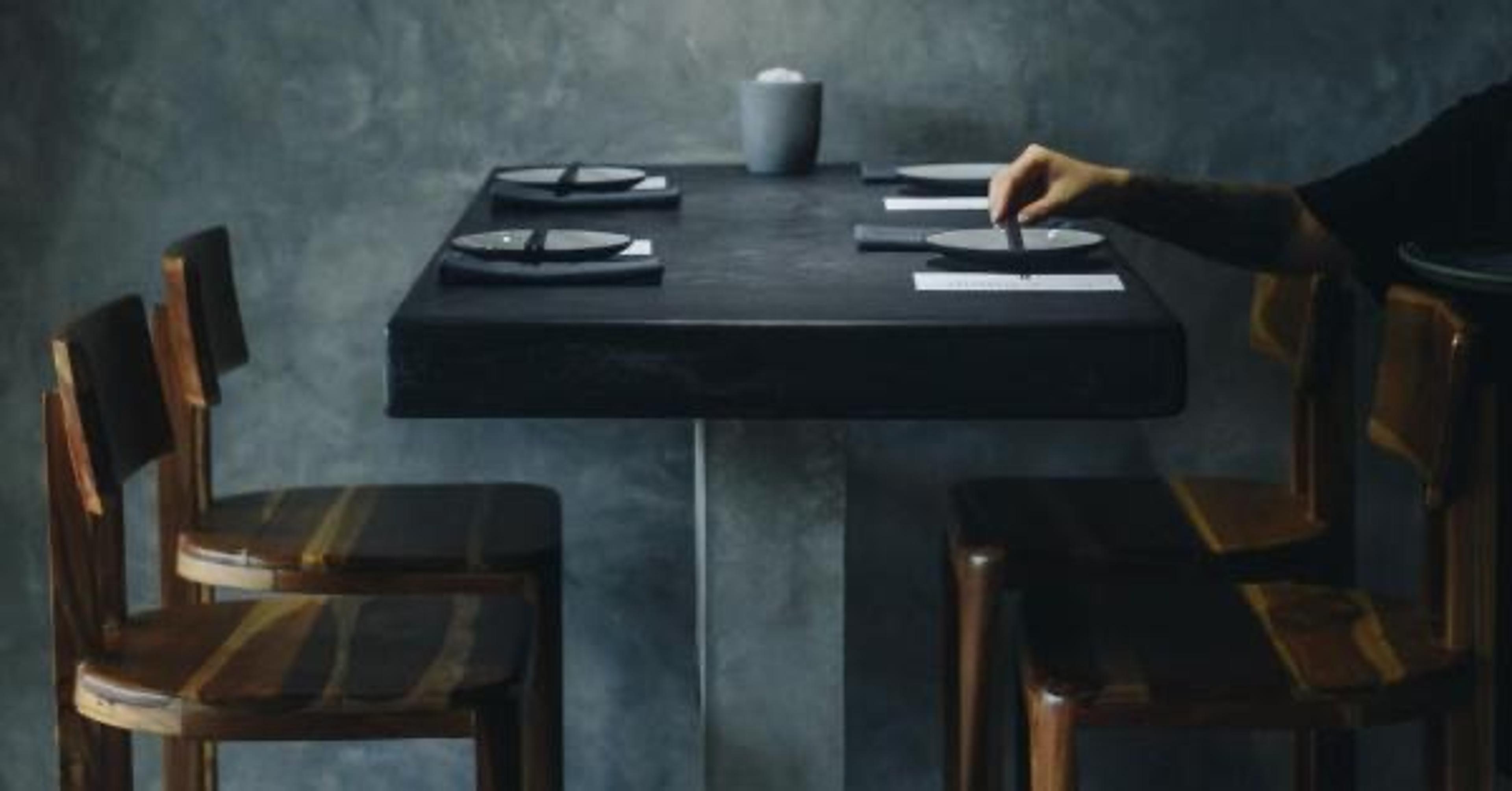 A dark concrete table laid with two place settings and chopsticks, in a grey room