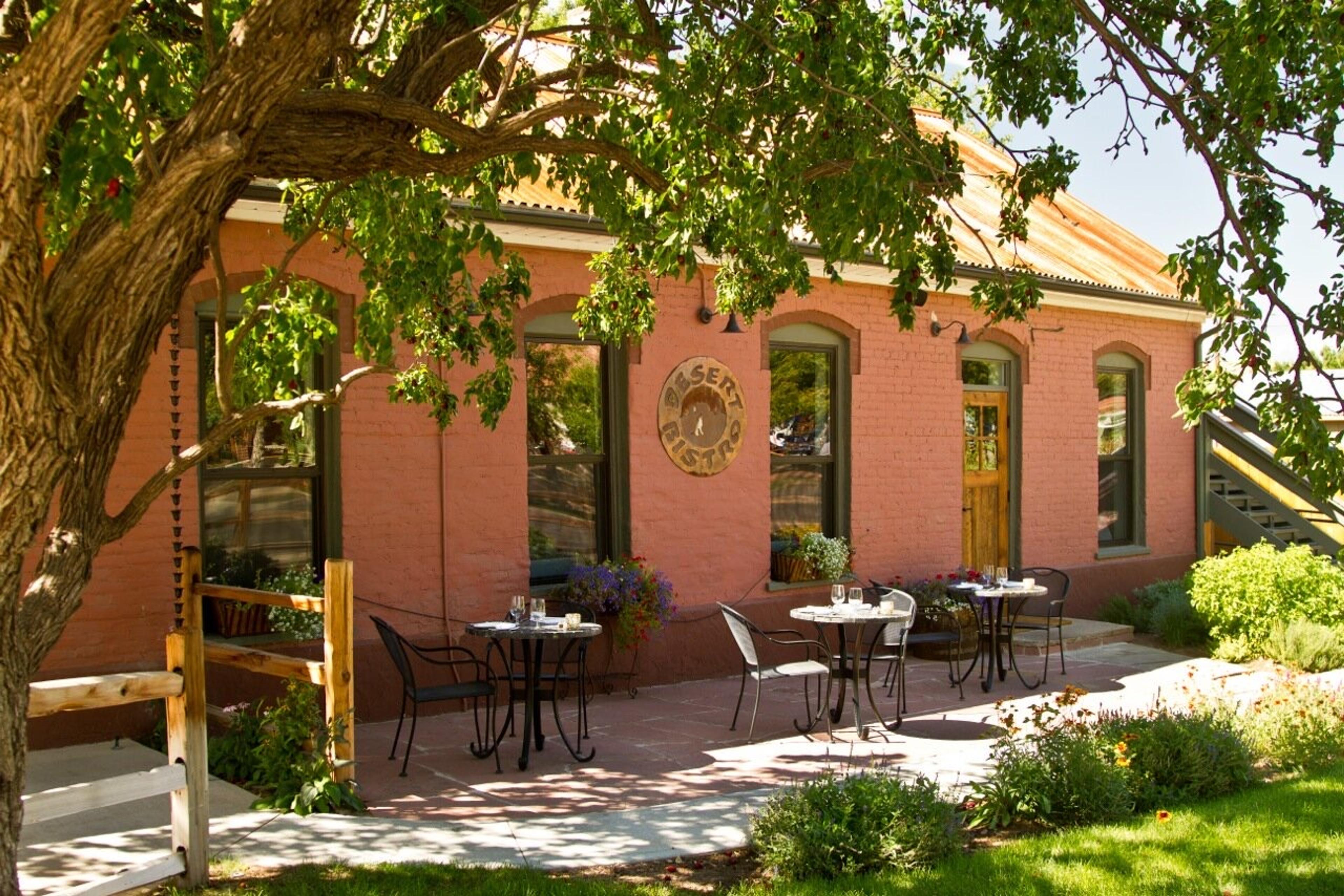 Tables on a garden patio in front of an old brick house under a shade tree