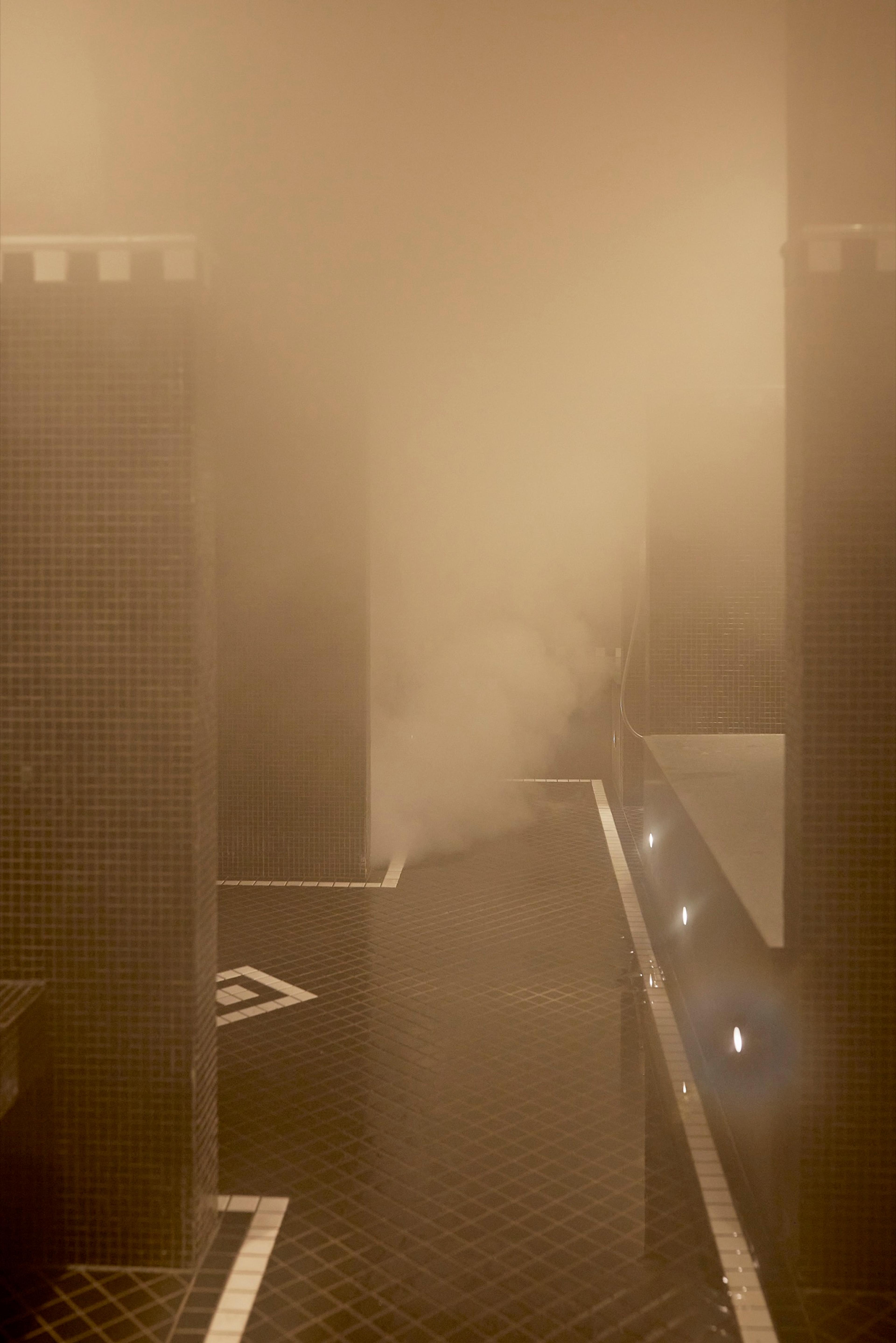 Steam fills a tiled room with square pillars and a dark tiled floor marked with pale inlaid lines.